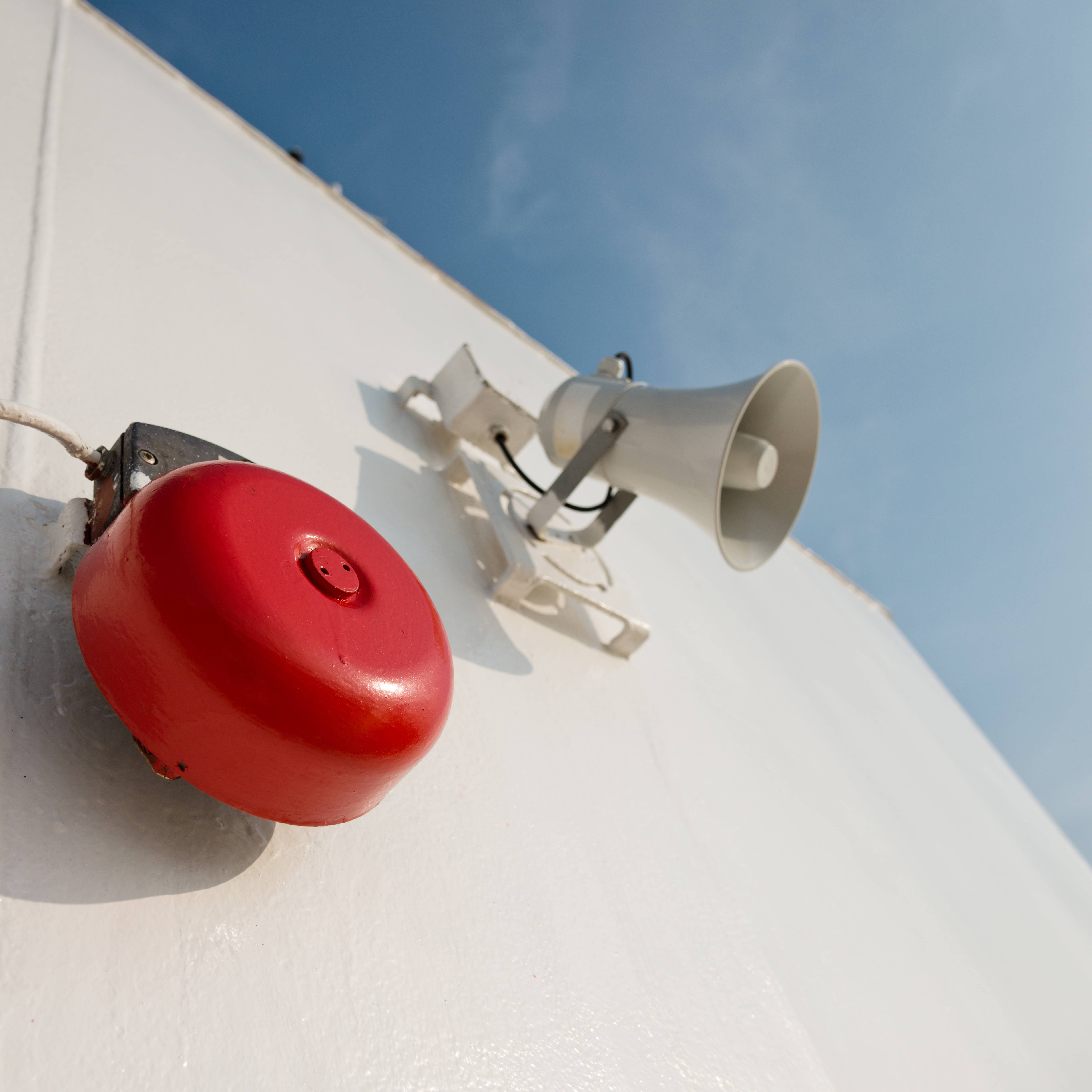 Außenwand mit roter Alarmglocke und weißem Trichterlautsprecher als Bestandteil einer Alarmanlage.