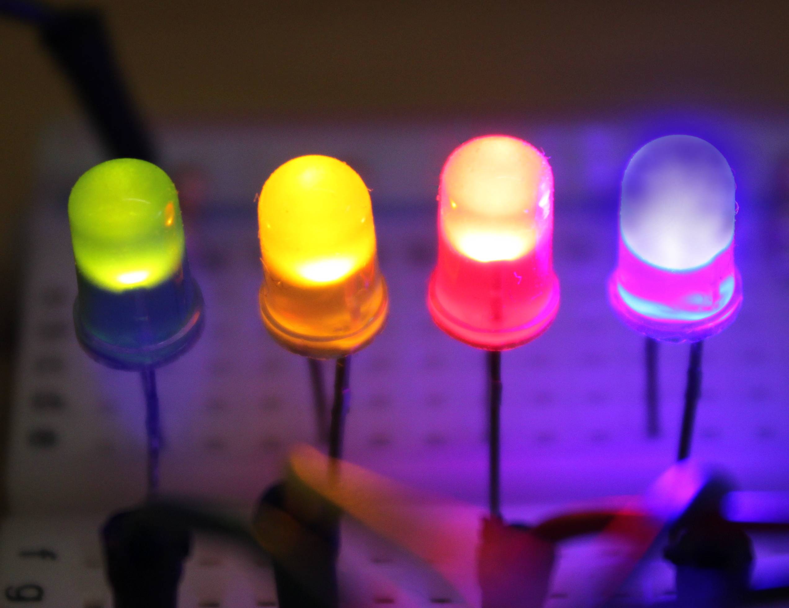 Nahaufnahme von vier leuchtenden LEDs in den Farben Grün, Gelb, Rot und Violett auf einer Platine.