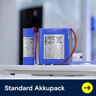 Zwei blaue Standard Akkupacks, ein zylindrischer und ein rechteckiger, mit Anschlusskabeln auf weißer Oberfläche.
