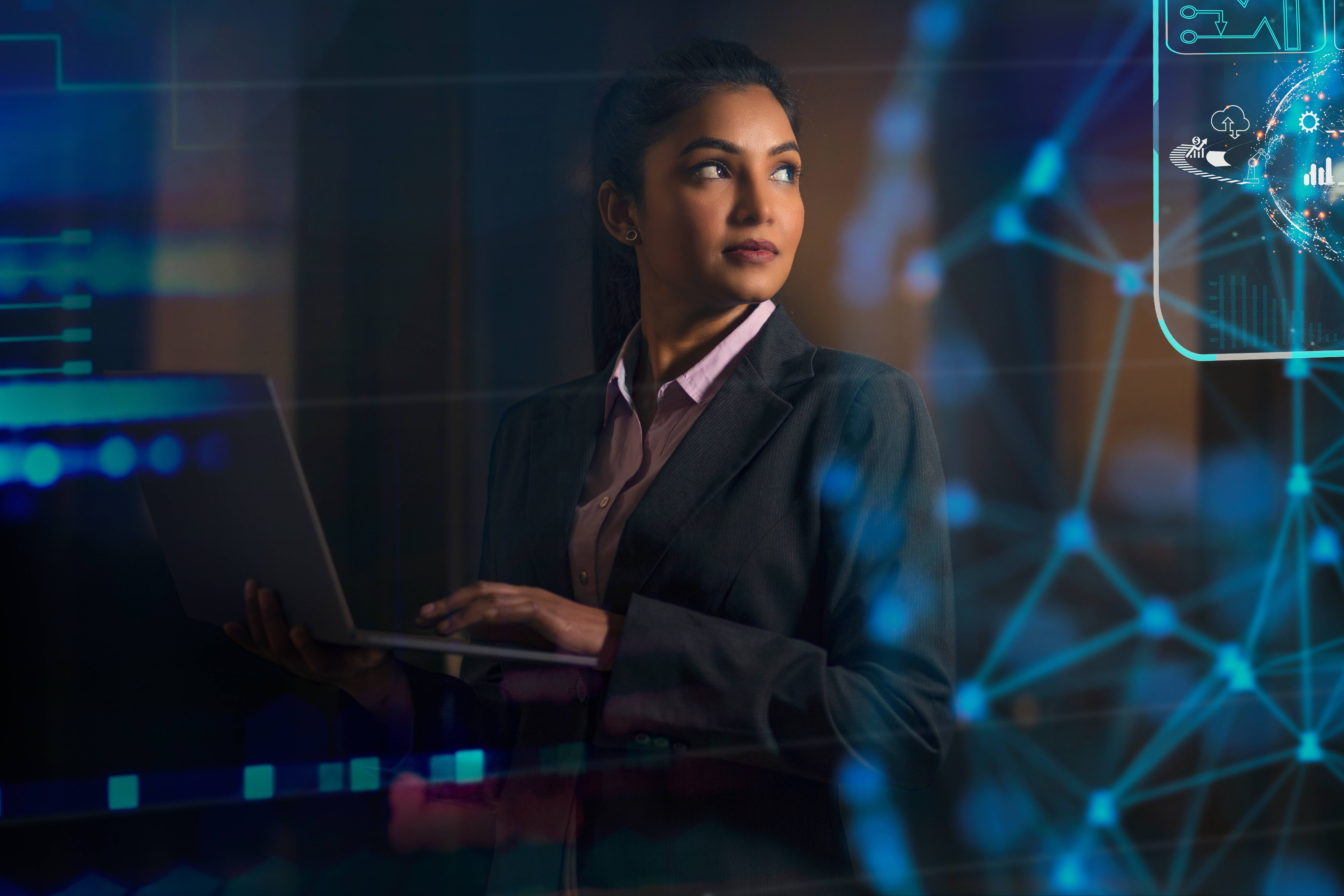 Auf dem Bild sieht man eine Frau mit einem Laptop. Es spannt sich ein blaues Netz durch den dunklen Hintergrund