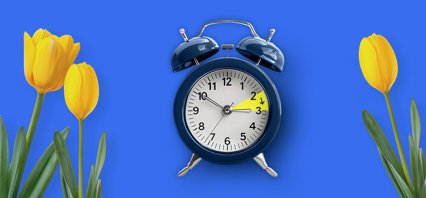 Ein blauer Wecker mit gelben Tulpen auf hellblauem Hintergrund. Der Zeiger vom Wecker zeigt auf 3 Uhr. Es sind 3 gelbe Tulpen im Bild zu sehen.