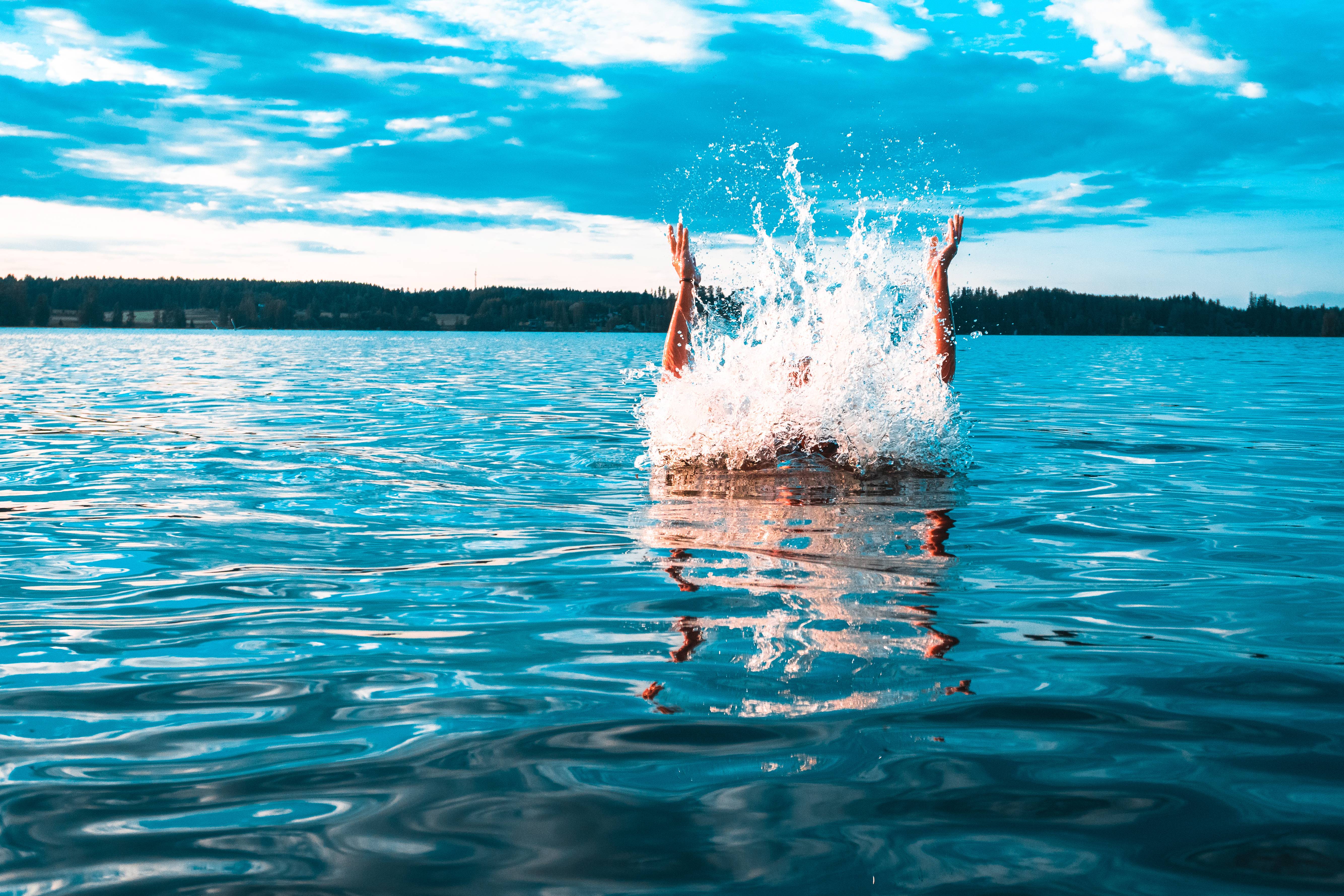 Person ist mit hochgeworfenen Armen ins Wasser gesprungen.