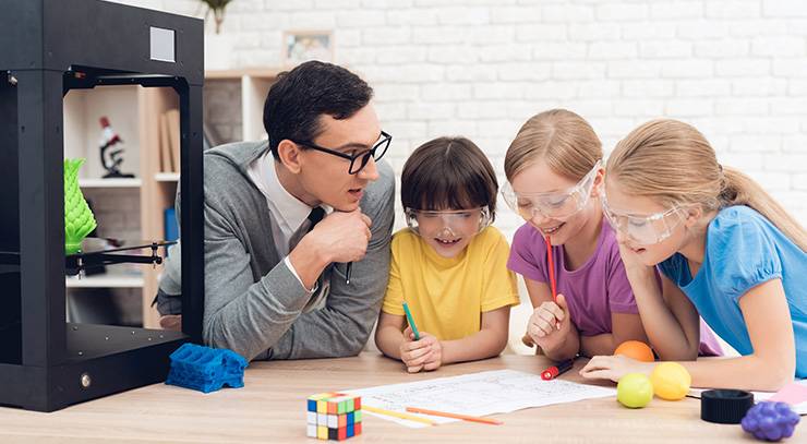 Lehrer und Kinder mit Schutzbrillen arbeiten gemeinsam an einem Technikprojekt mit 3D-Drucker.