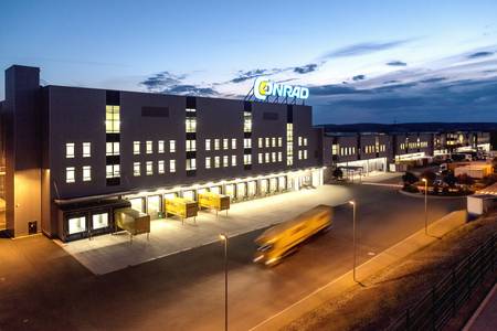 Conrad Logistikzentrum LOC nachts, beleuchtet, mit Laderampen und vorbeifahrendem Fahrzeug.