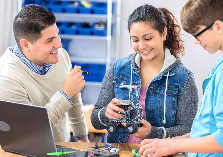 Trois jeunes travaillent ensemble sur un petit robot dans une salle technique.