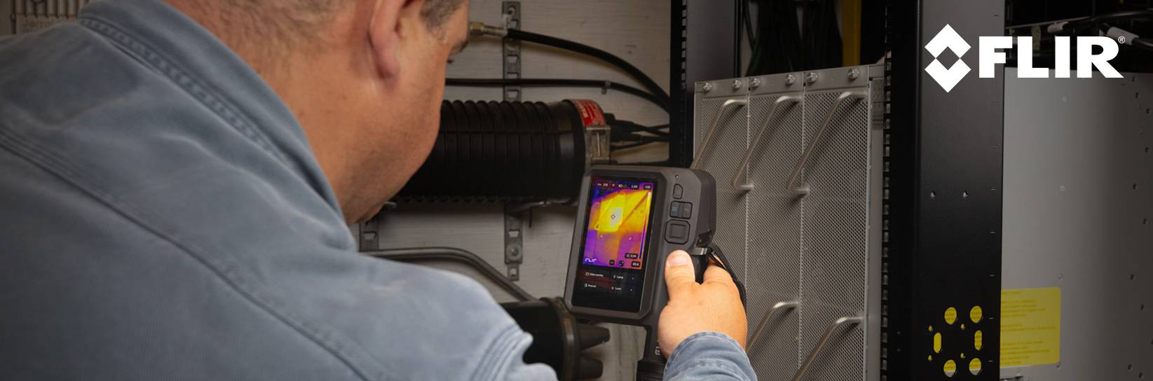 Mann prüft Schaltschrank mit Flir Wärmebildkamera.