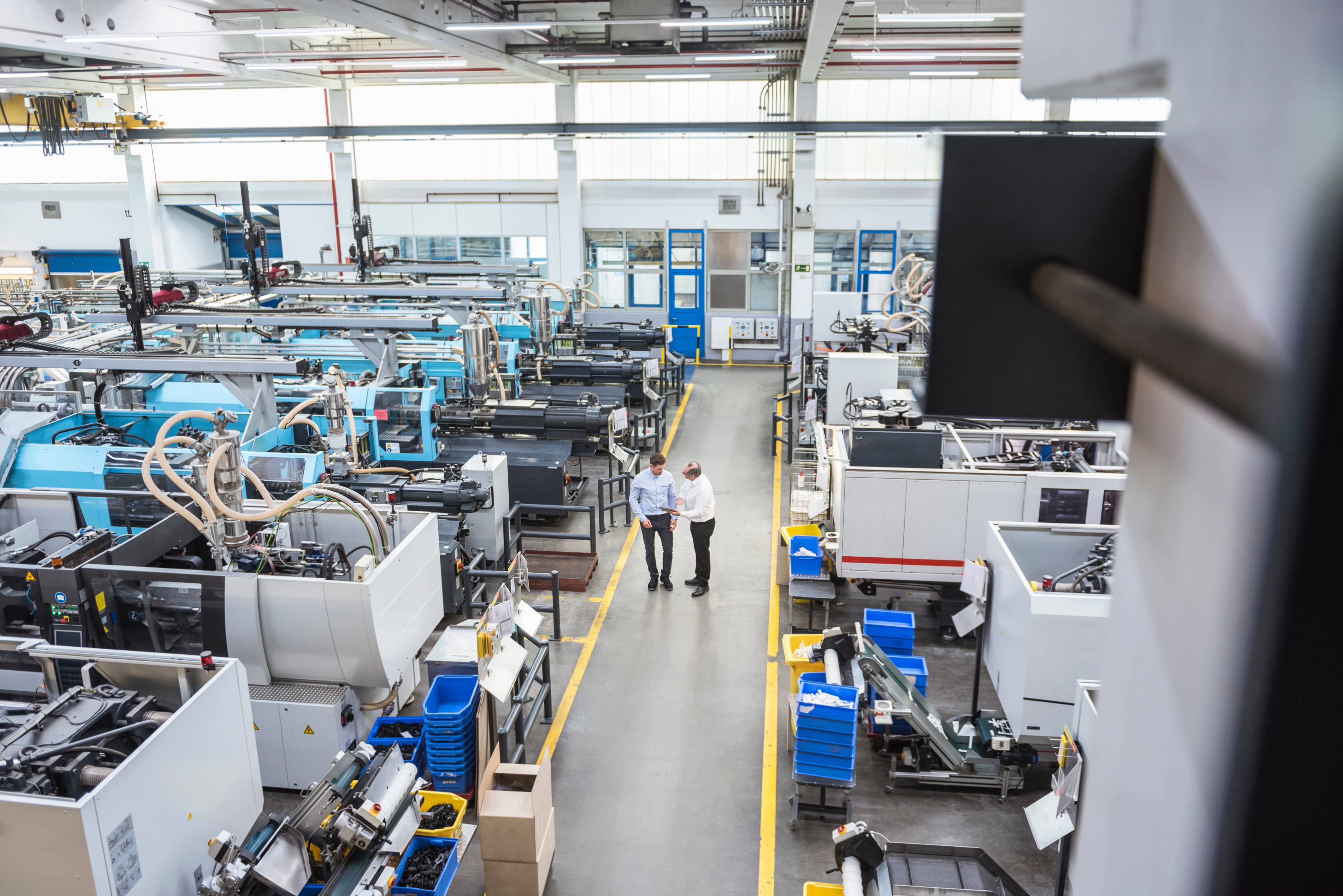 Zwei Männer gehen durch eine große Industriehalle mit Maschinen und Produktionsanlagen.