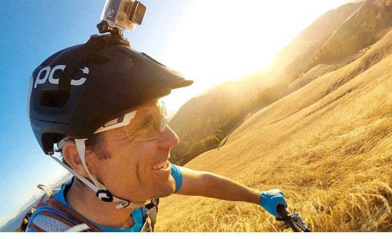 Mann mit Fahrradhelm und Actionkamera fährt bei Sonnenuntergang durch eine hügelige Landschaft.
