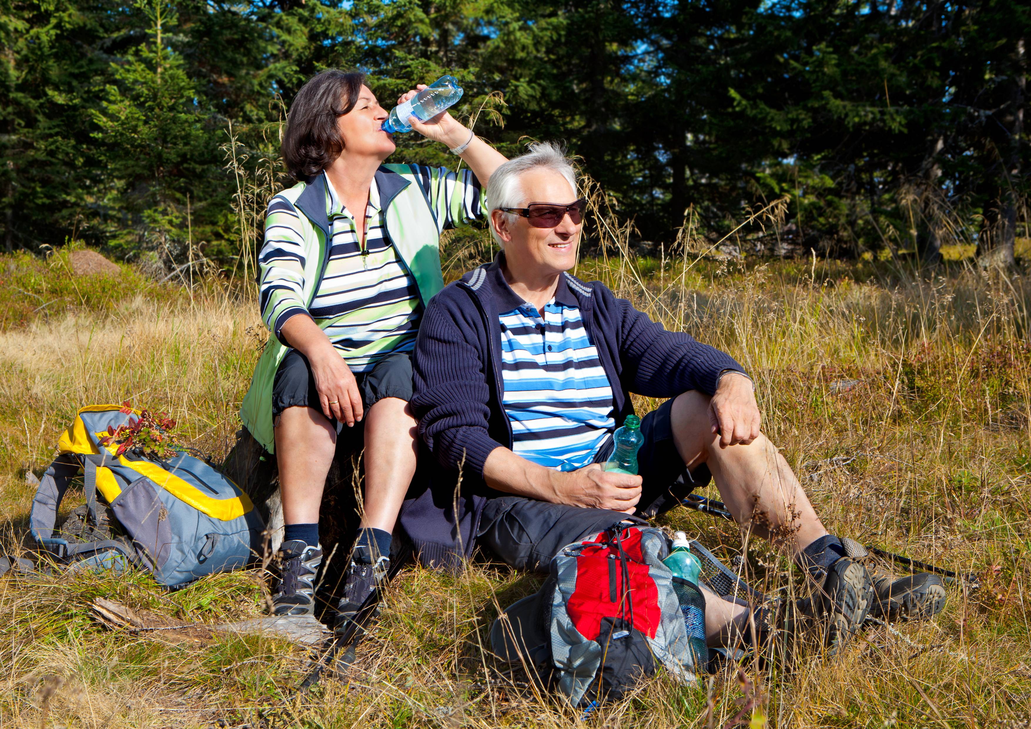 Älteres Paar macht Rast beim Wandern, sitzt in der Wiese und trinkt Wasser.