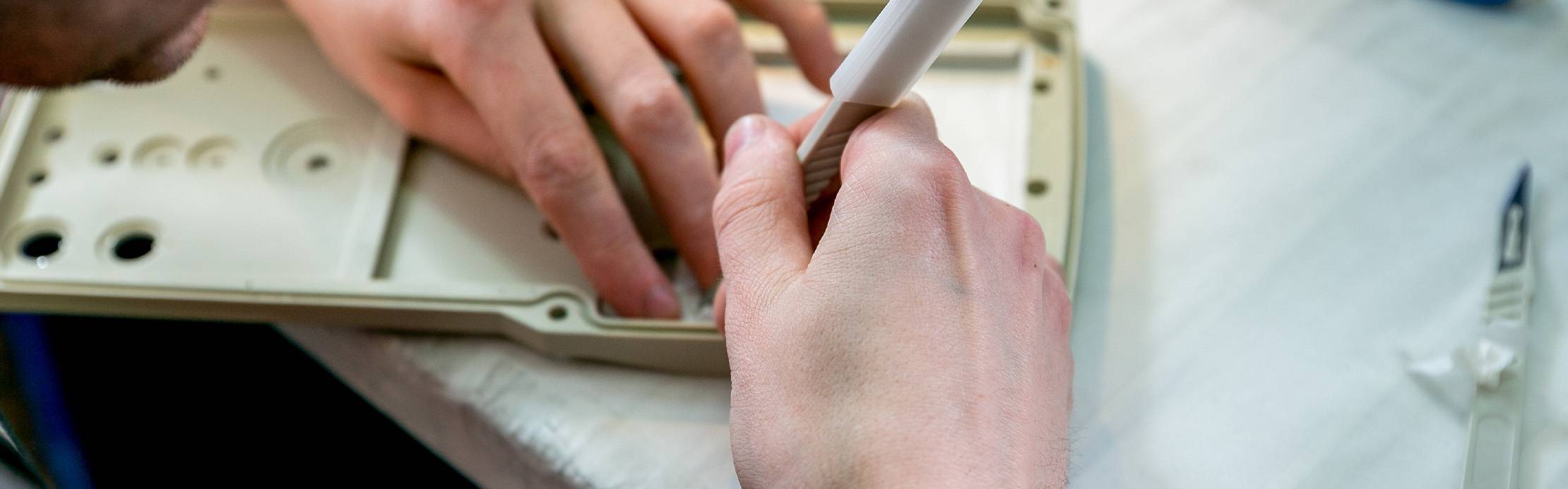 Eine Person bearbeitet mit einem Handwerkzeug präzise ein Kunststoffgehäuse für einen Prototypen.