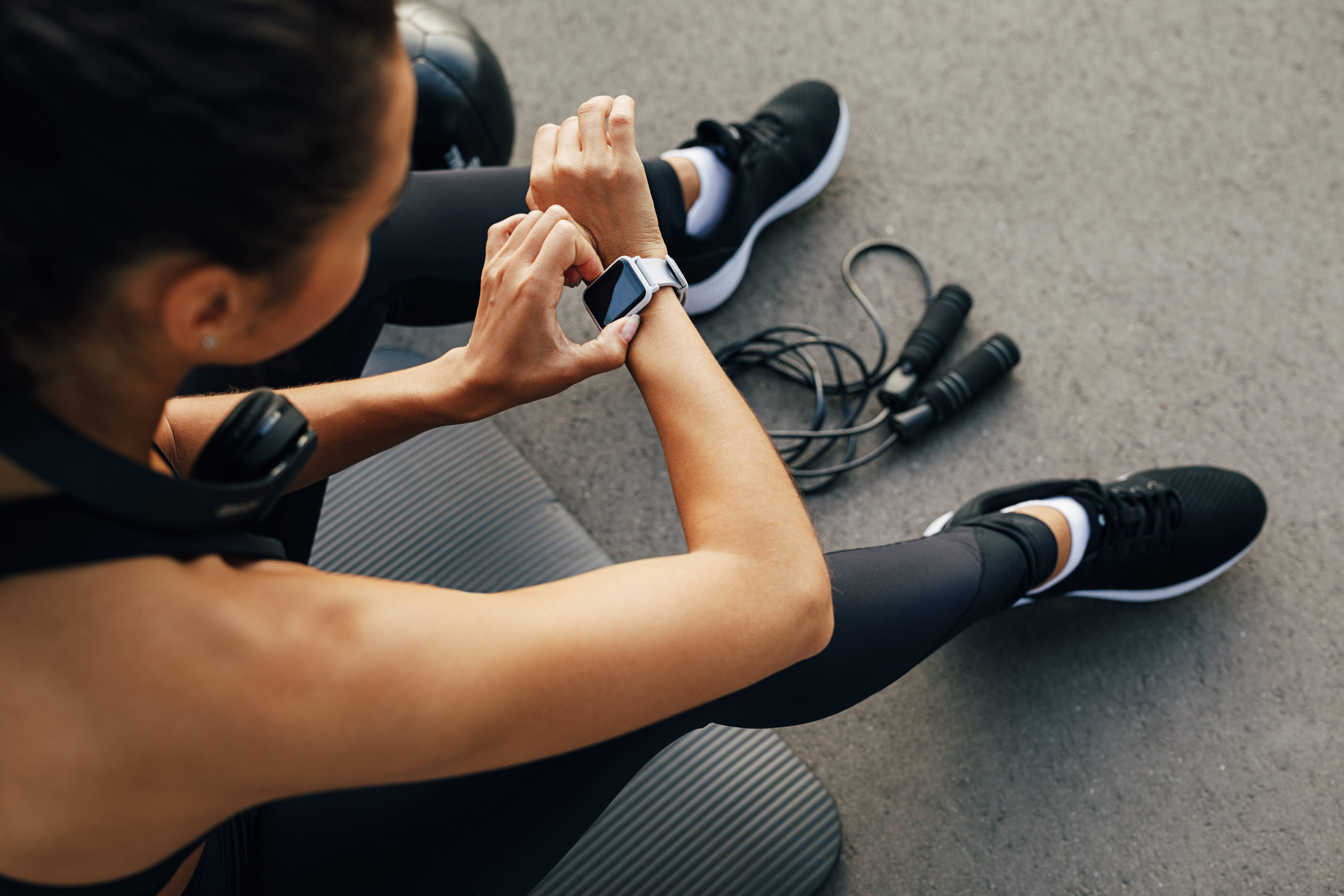 Eine Frau in Sportkleidung überprüft ihre Smartwatch nach dem Training mit einem Springseil.