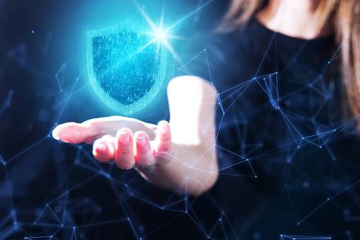Symbol für Datensicherheit im Büro: Ein leuchtendes digitales Schutzschild-Icon über einer Hand visualisiert den Schutz sensibler Informationen.