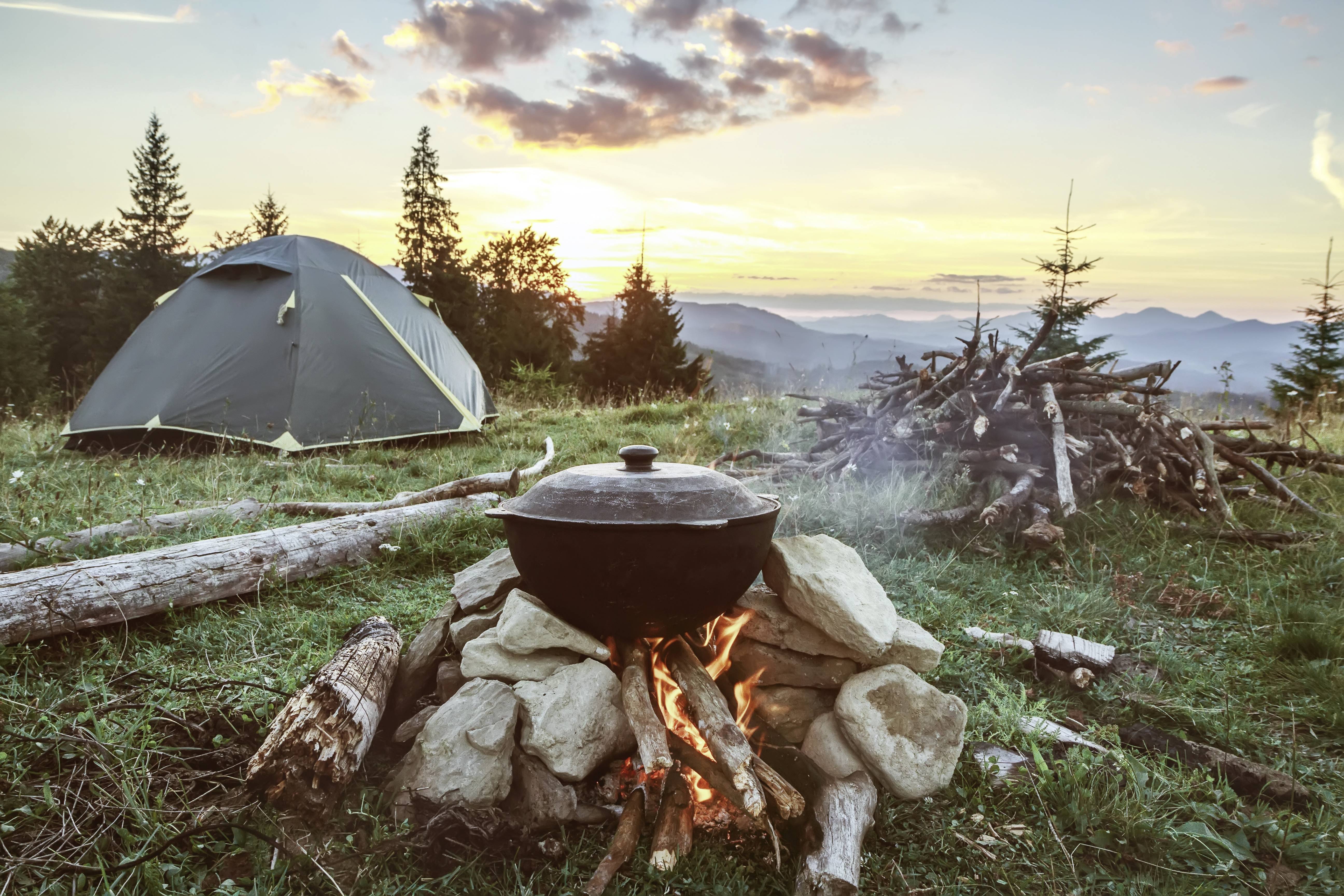 Zelt und Lagerfeuer mit Kochtopf in den Bergen bei Sonnenuntergang.