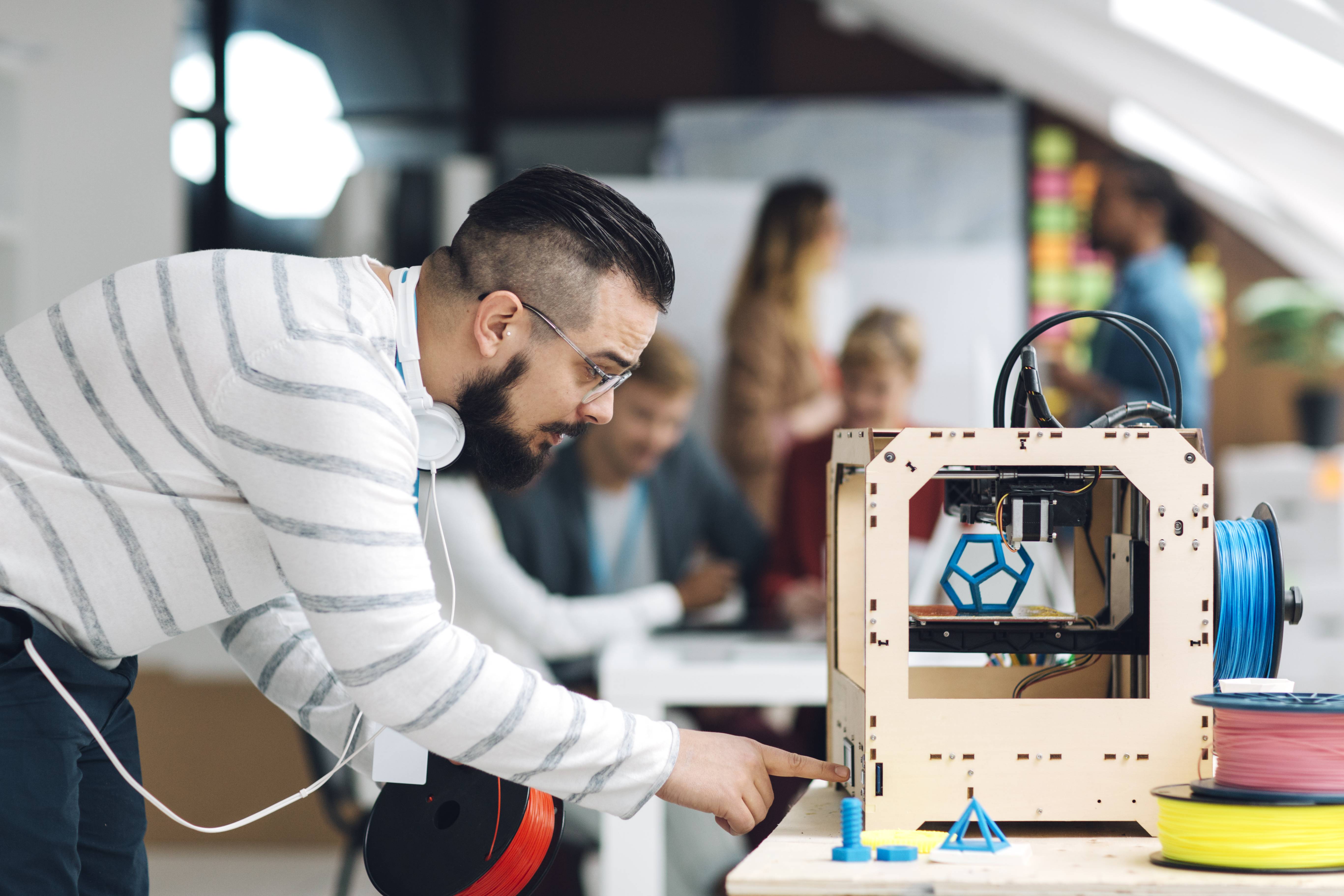Ein Mann mit Kopfhörer kontrolliert gerade den Druck seines 3D-Druckers