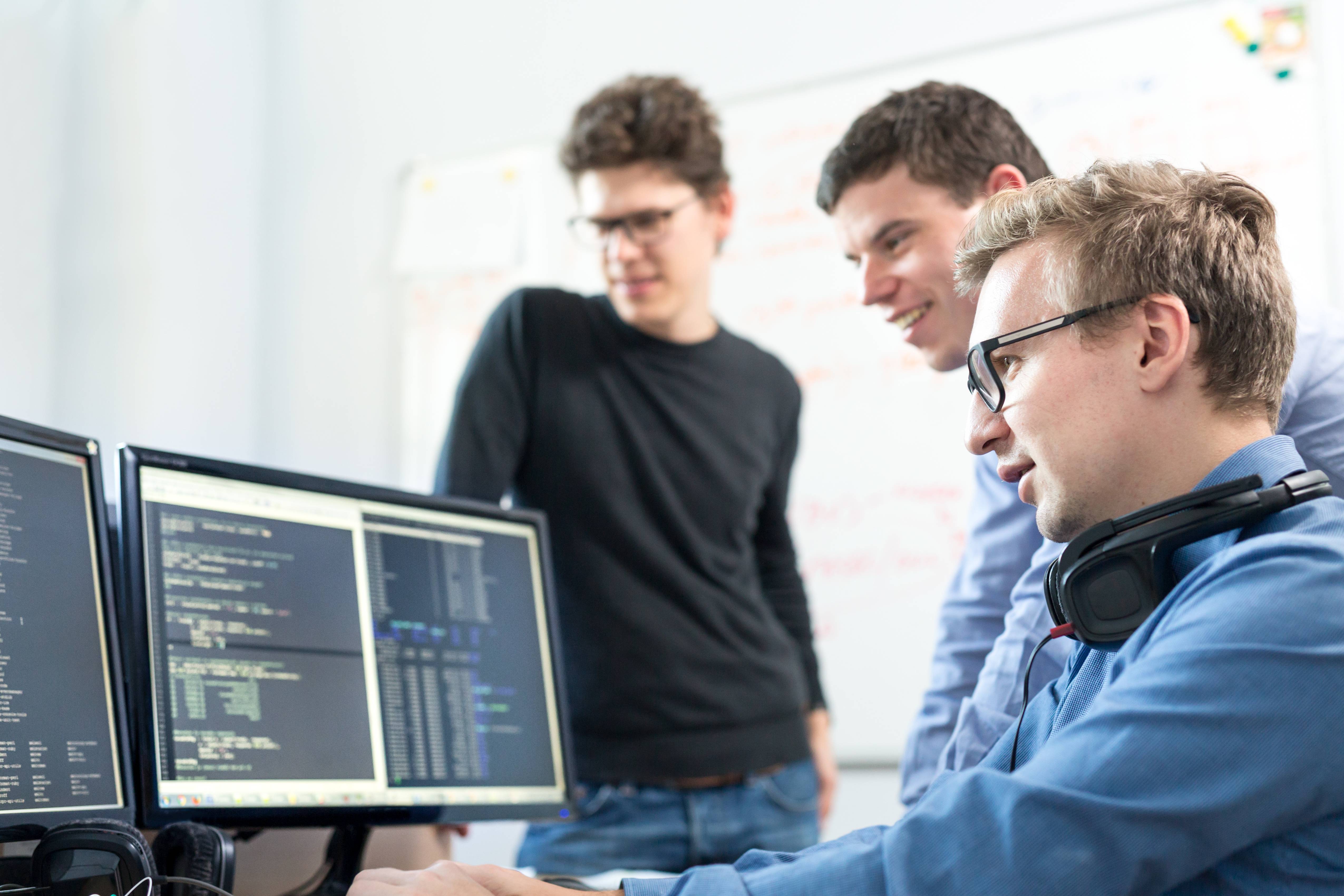 Auf dem Bild sind drei Menschen zu sehen, die auf einen Monitor schauen.