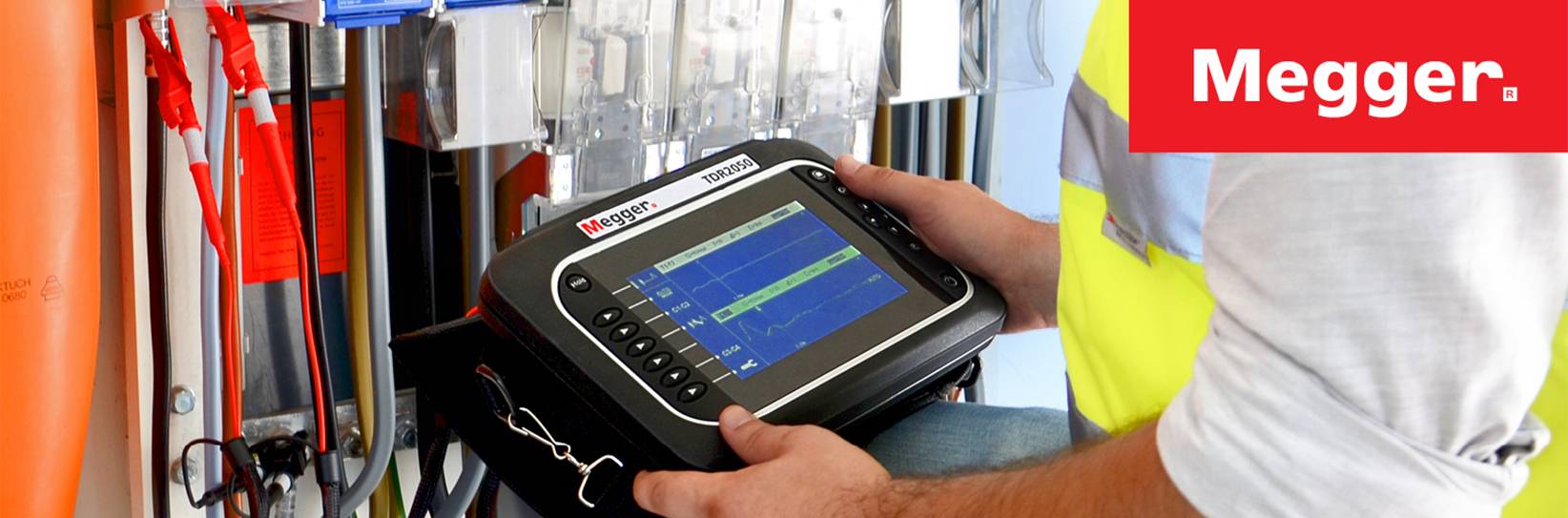 Megger: Techniker hält Messgerät vor Elektroinstallation.