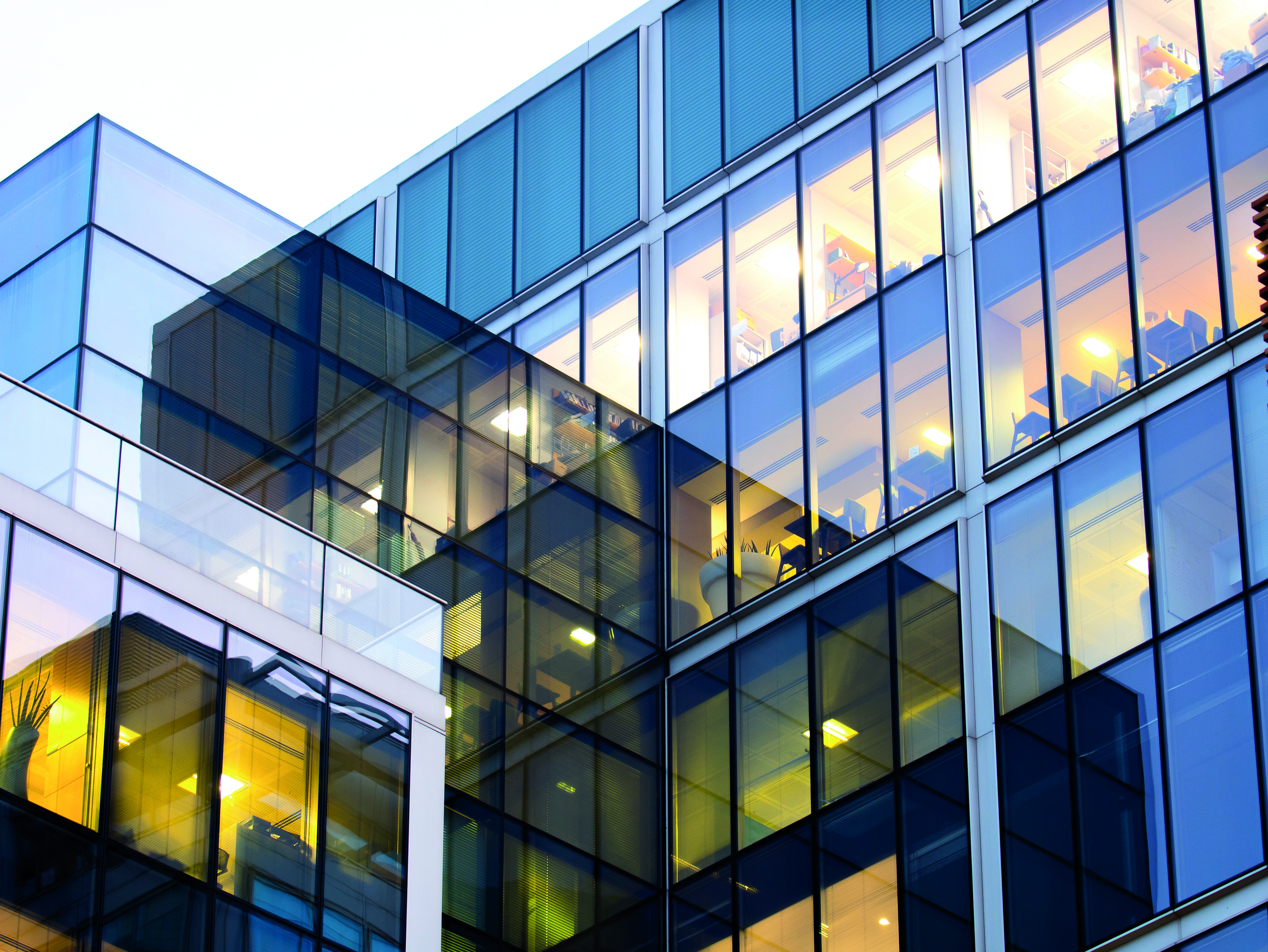 Modernes Bürogebäude mit Glasfassade und erleuchteten Innenräumen am Abend.