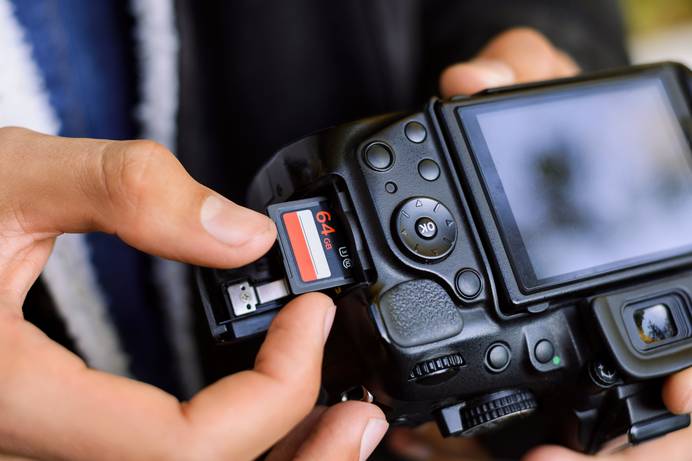 Man sieht in Nahaufnahme, wie eine Person eine 64-GB-Speicherkarte in eine Fotokamera einlegt. Das Gerät ist scheinbar ausgeschaltet, da auf dem Display nichts zu sehen ist.