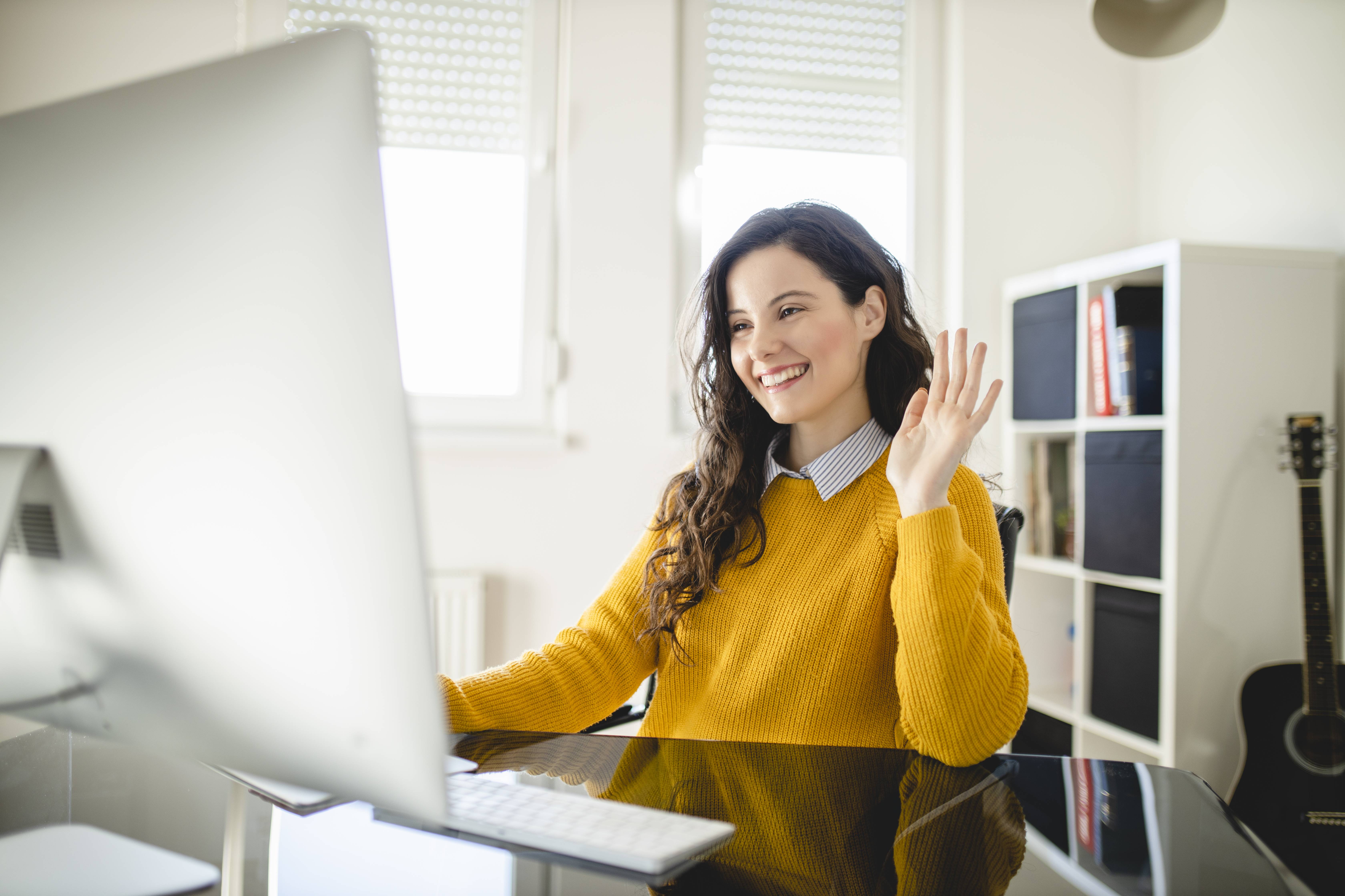Professioneller Arbeitsplatz im Homeoffice: Eine lächelnde Mitarbeiterin führt eine Videokonferenz an einem modernen Desktop-PC.