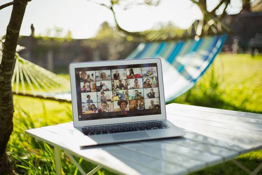 Laptop im Garten auf weißem Tisch zeigt eine große Videokonferenz in Kachelansicht (Online-Meeting).