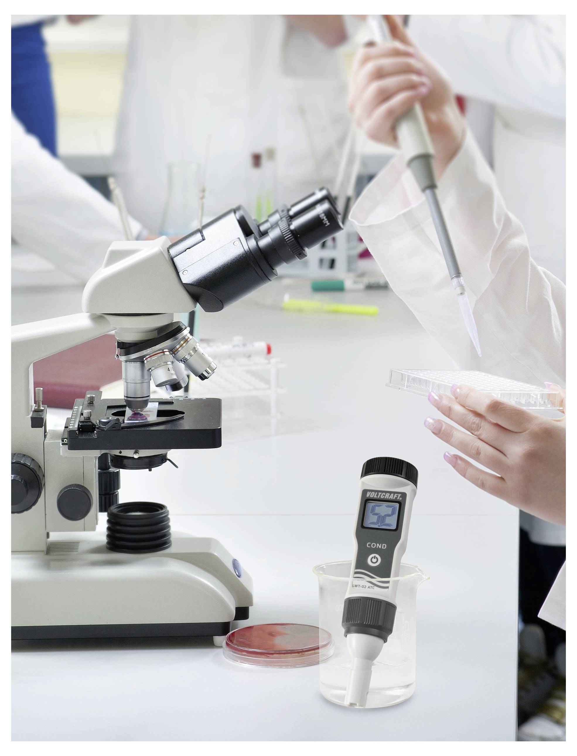 Laboratorní prostředí s mikroskopem, rukama používajícíma pipetu a digitálním zařízením zobrazujícím '2.00'.