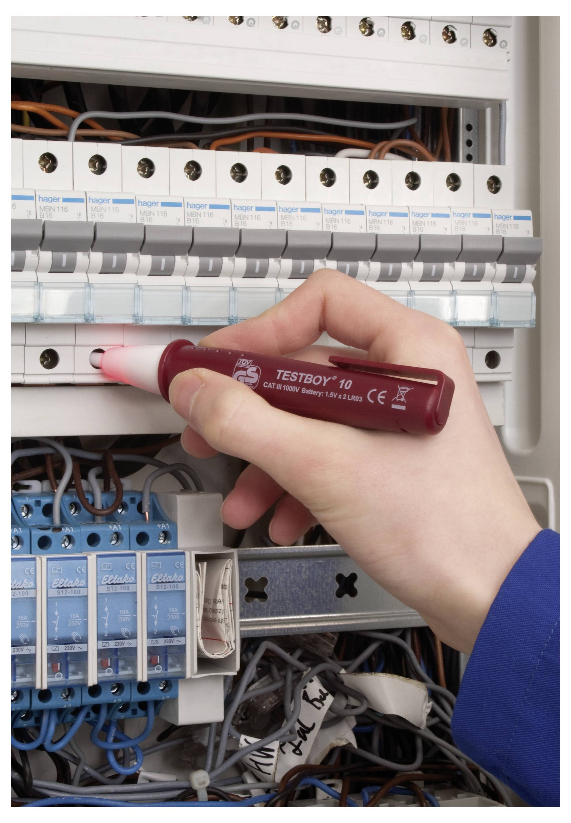 Osoba používá tester napětí v elektrickém rozvaděči a kontroluje obvody. Rozvaděč má viditelné mehreatické jističe a vodiče.