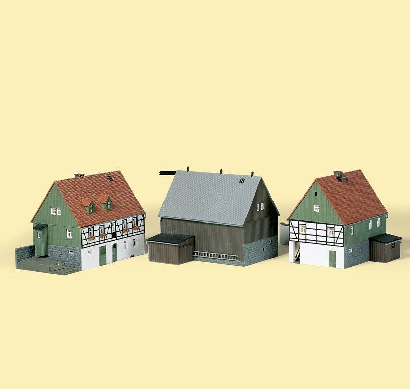 Tři modelové budovy s německou architekturou: dva zelené domy se zřízením v halových konstrukcích s červenými střechami a jedna šedá průmyslová budova.