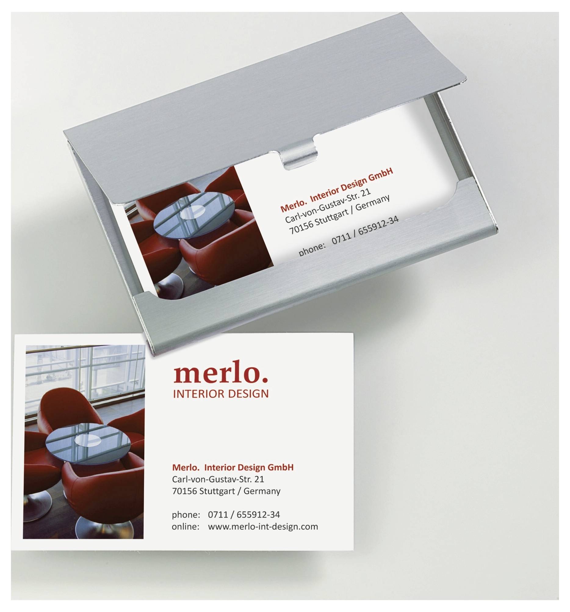 Vizitka a kovový držák na vizitky pro 'Merlo Interior Design GmbH' zobrazující logo, fotografii kanceláře, adresu ve Stuttgartu, telefonní číslo a webové stránky.