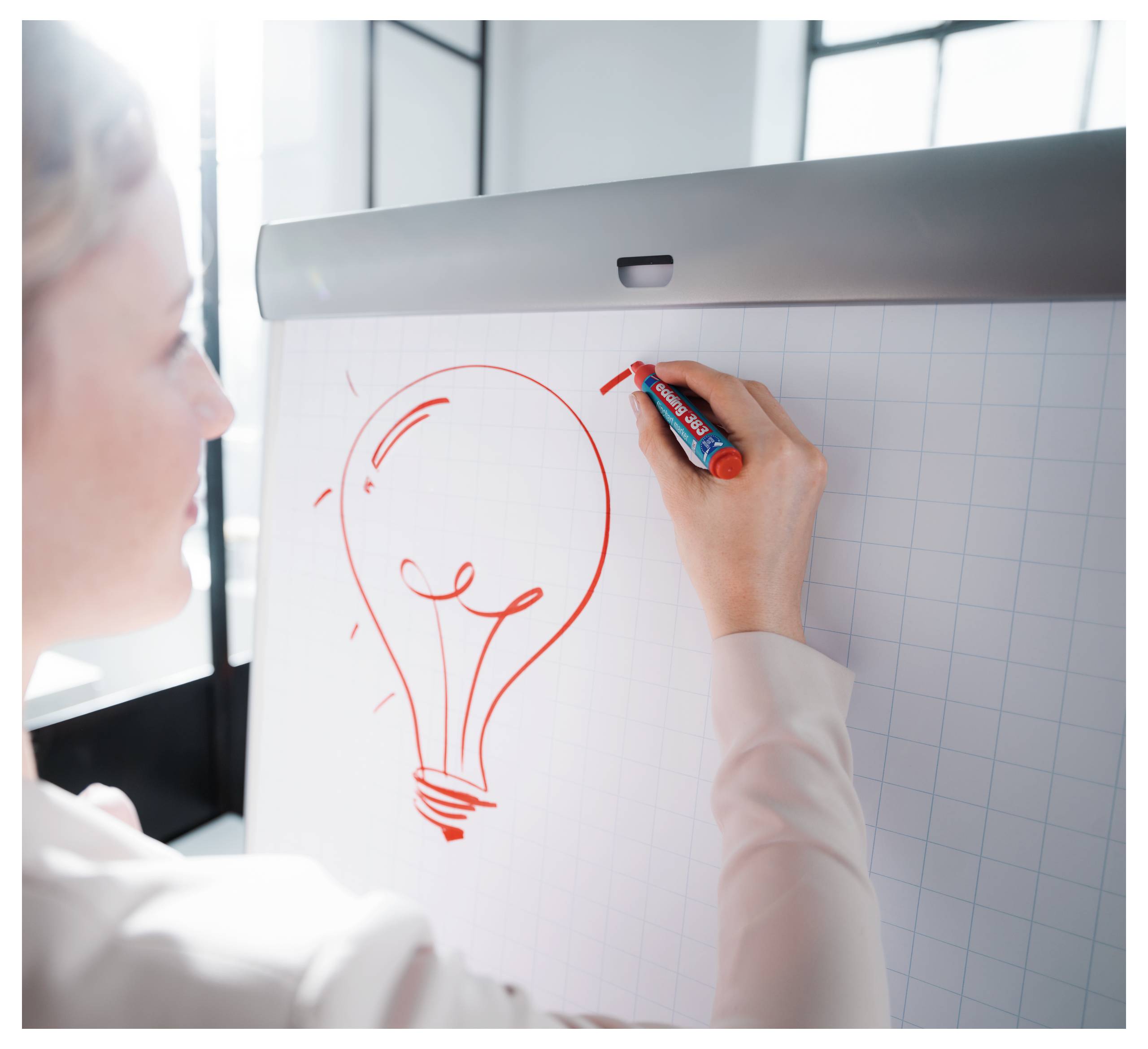 Osoba kreslící ikonu žárovky na flipchart, naznačující brainstorming nebo nový nápad.