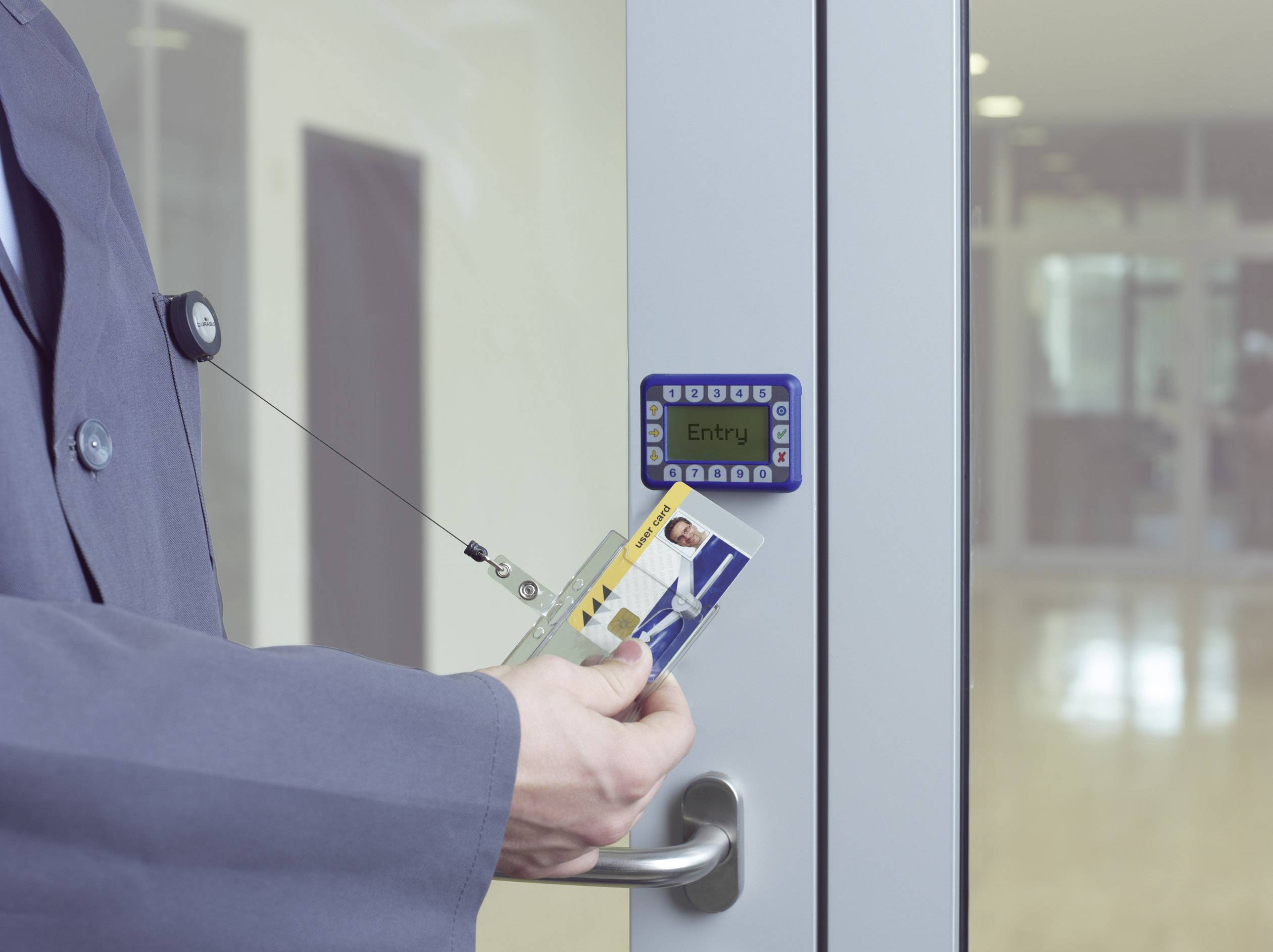 Osoba přiloží RFID kartu ke čtečce přístupového kontrolního zařízení na skleněných dveřích, aby získala přístup do budovy.