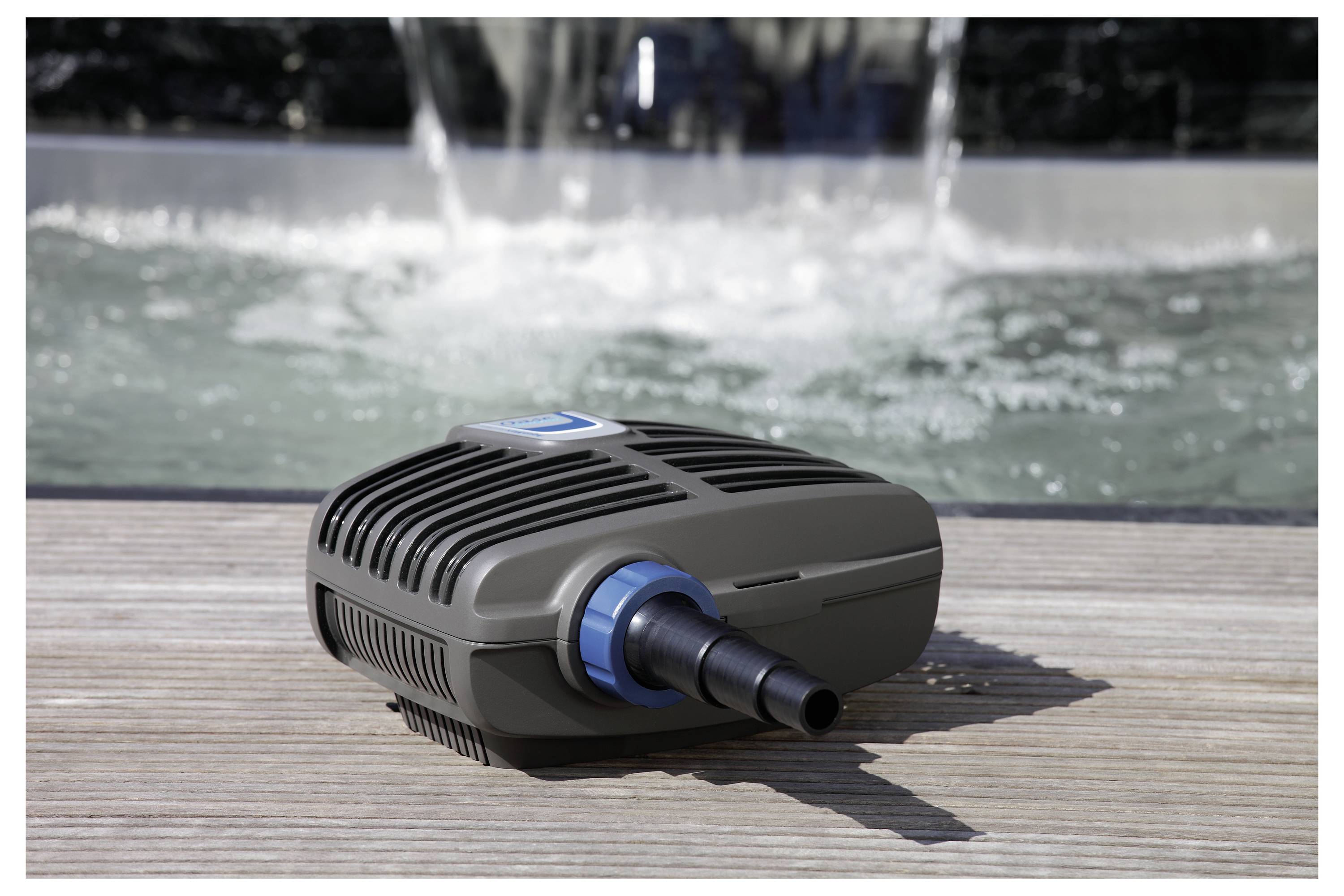 Malá černá zahradní pumpa s modrou tryskou, umístěná na dřevěné terase před rozostřeným vodním prvkem.