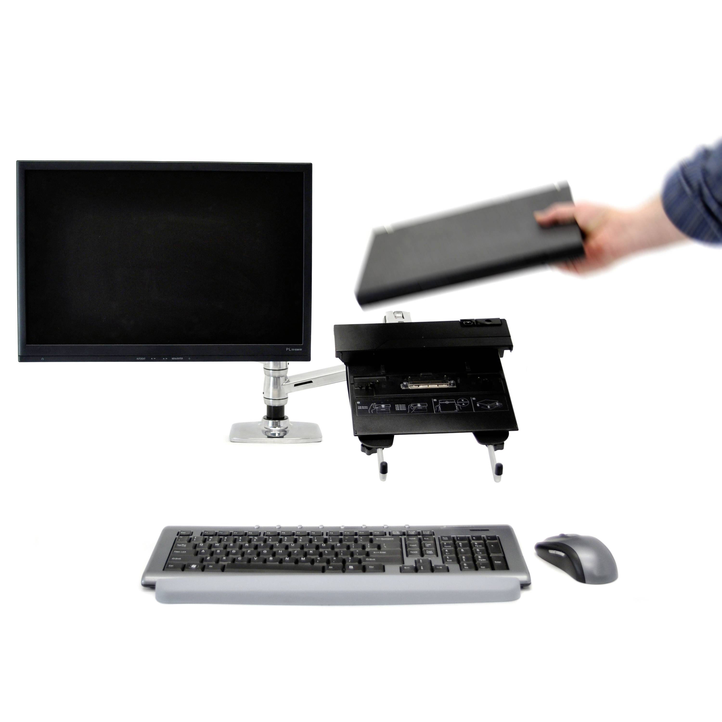 Pracoviště s monitorem, klávesnicí a myší. Osoba drží zavřený notebook.
