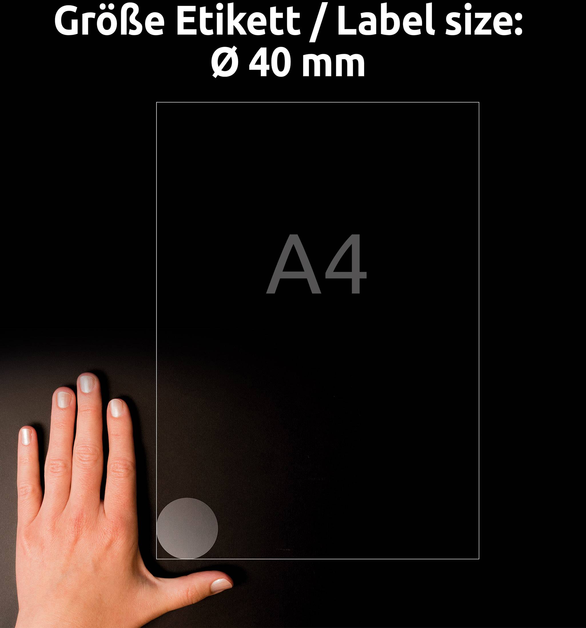 Lidská ruka ukazuje na štítek o průměru 40 mm, který leží na průhledném listu formátu A4.
