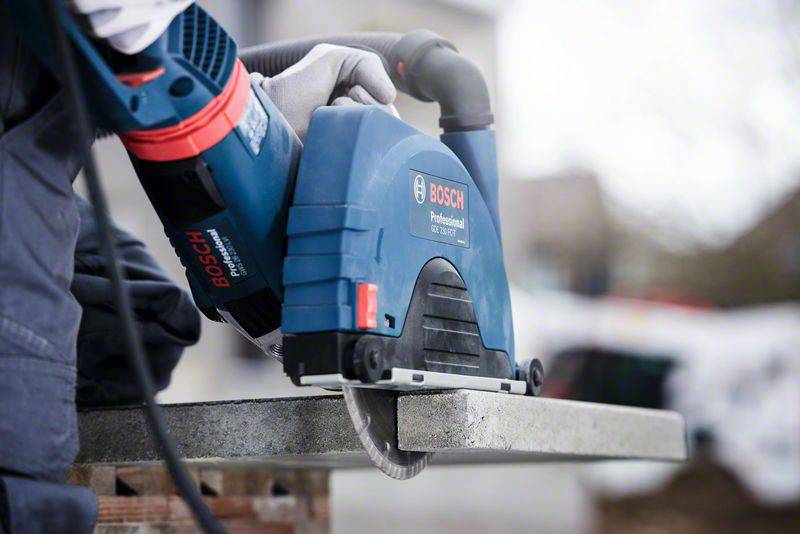 Osoba řeže kámen modrou kotoučovou pilou Bosch. Osoba má na sobě bezpečnostní oděv a okolí je rozostřené.