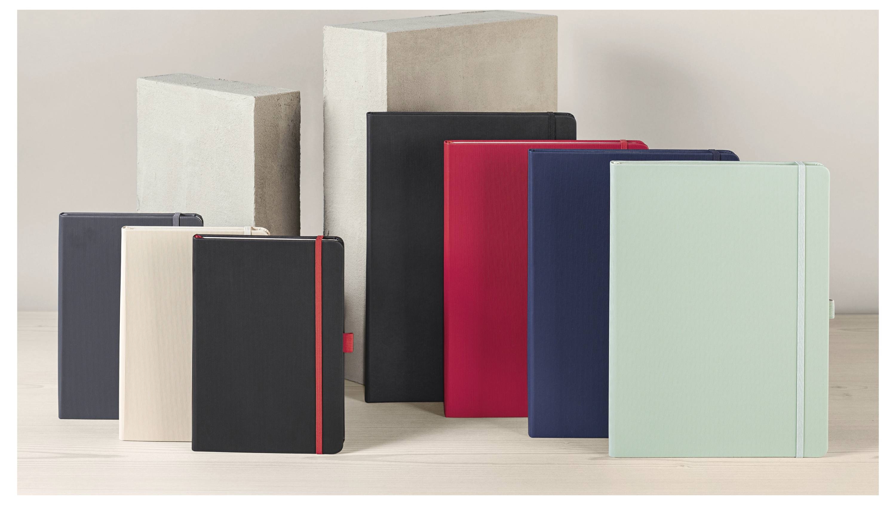 Několik zavřených notebooků nebo plánovačů v různých barvách je uspořádáno na světlém povrchu, s jedním v barvě máty zeleně v popředí.