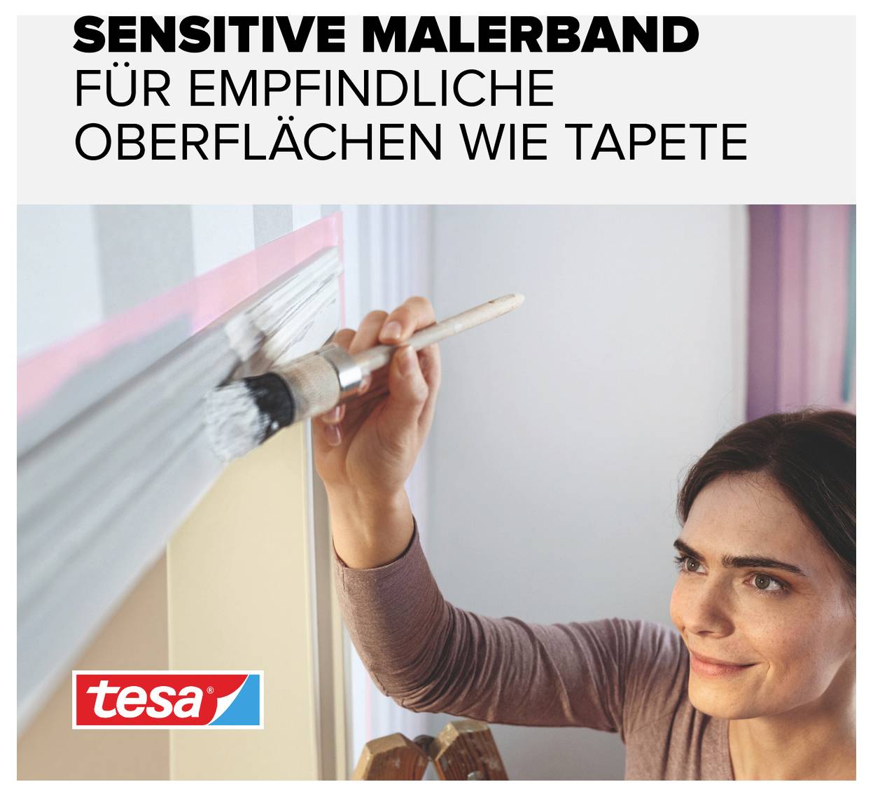 Žena nanáší bílou barvu štětcem na zeď; používá malířskou pásku 'tesa' pro citlivé povrchy, jako jsou tapety.