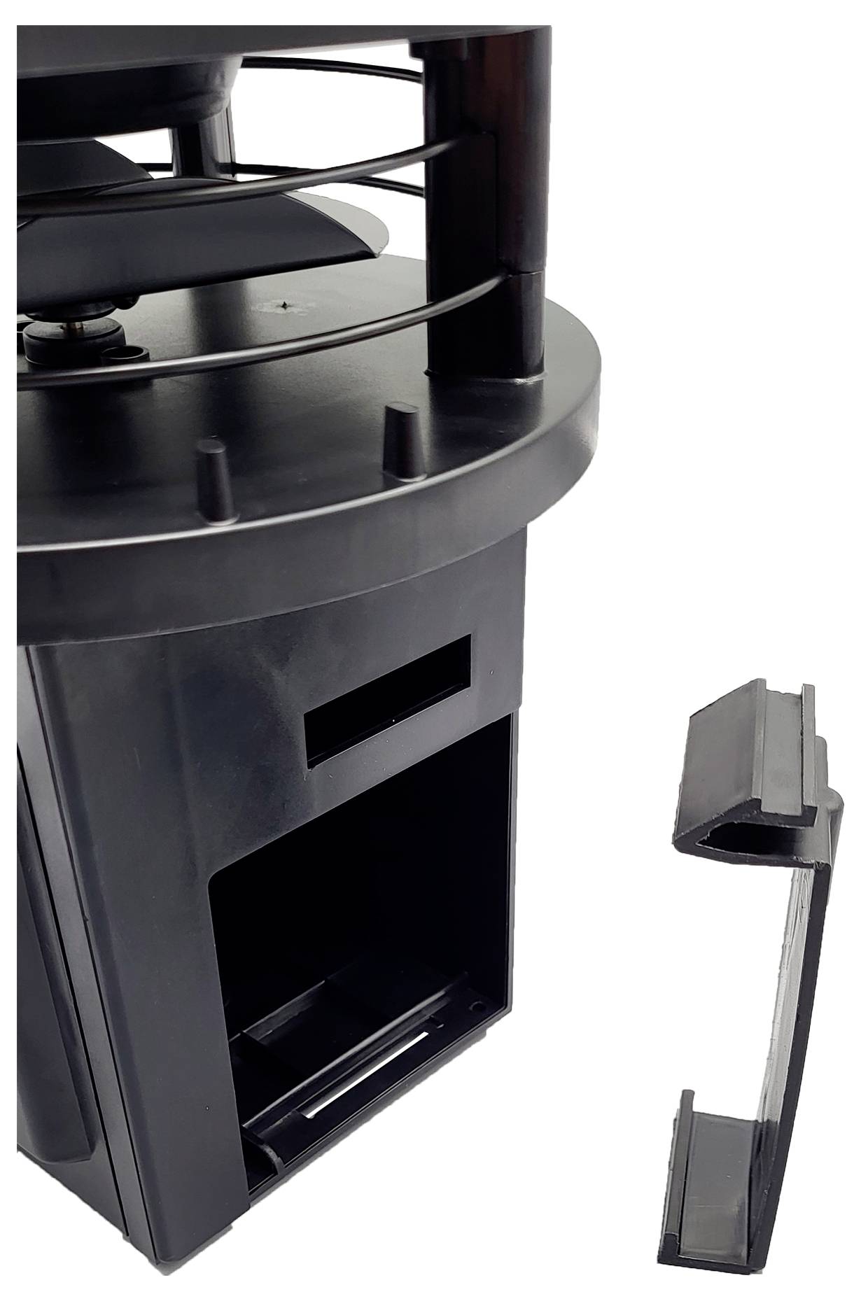 Černé mechanické zařízení s válcovitou horní sekcí, která má spirálovité pruty, a otevřeným prostorem dole, vedle něhož leží rozložené komponenty.