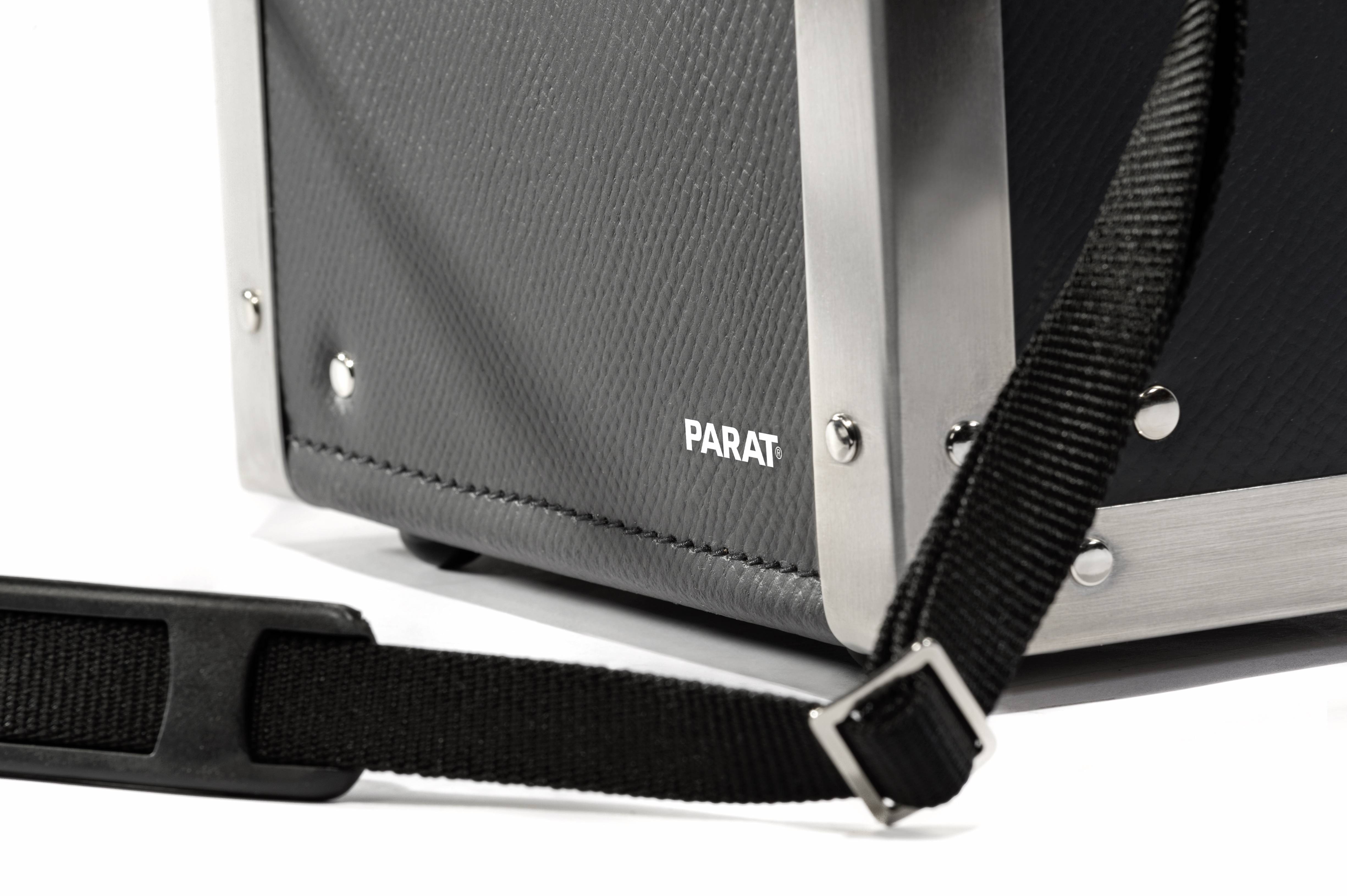 Detailní záběr černého strukturovaného pevného kufru s kovovým rámem a černým ramenním popruhem. Označení 'PARAT'.