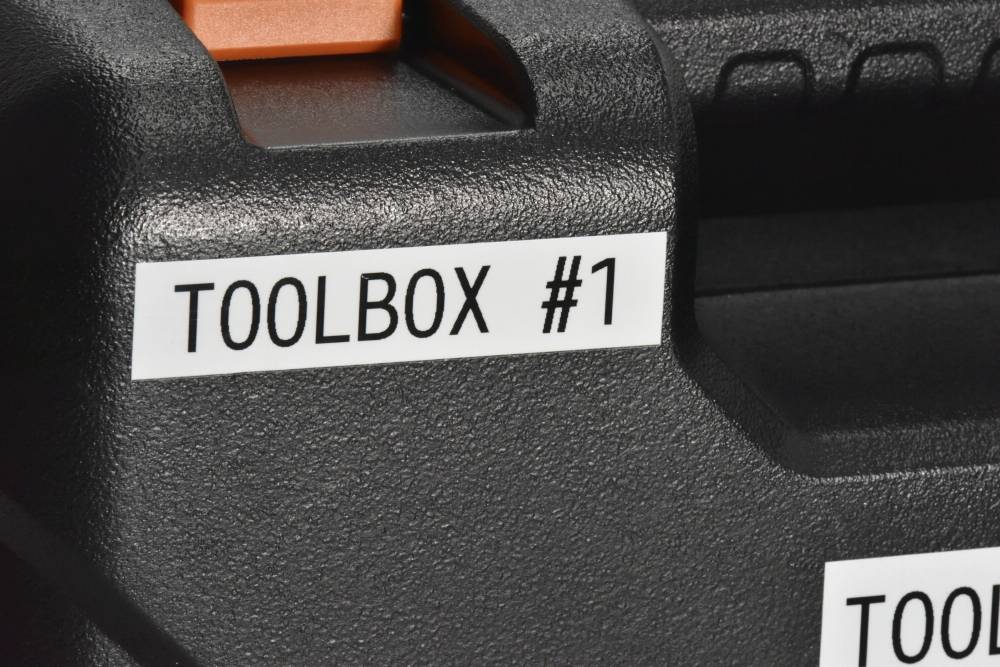 Černý kufřík na nářadí s textovou nálepkou 'TOOLBOX #1' vlevo nahoře, v detailním záběru.