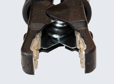 Detailní záběr na černý kovový krimpovací nástroj se zuby, který stiskuje malý kovový konektor.