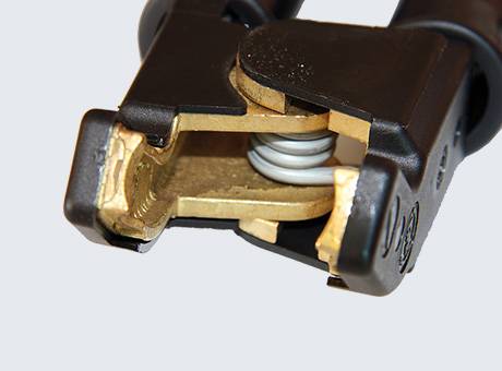 Detailní pohled na černou a mosaznou svorku kabelu s viditelným pružinovým mechanismem uvnitř, která se používá pro bezpečné elektrické spojení.
