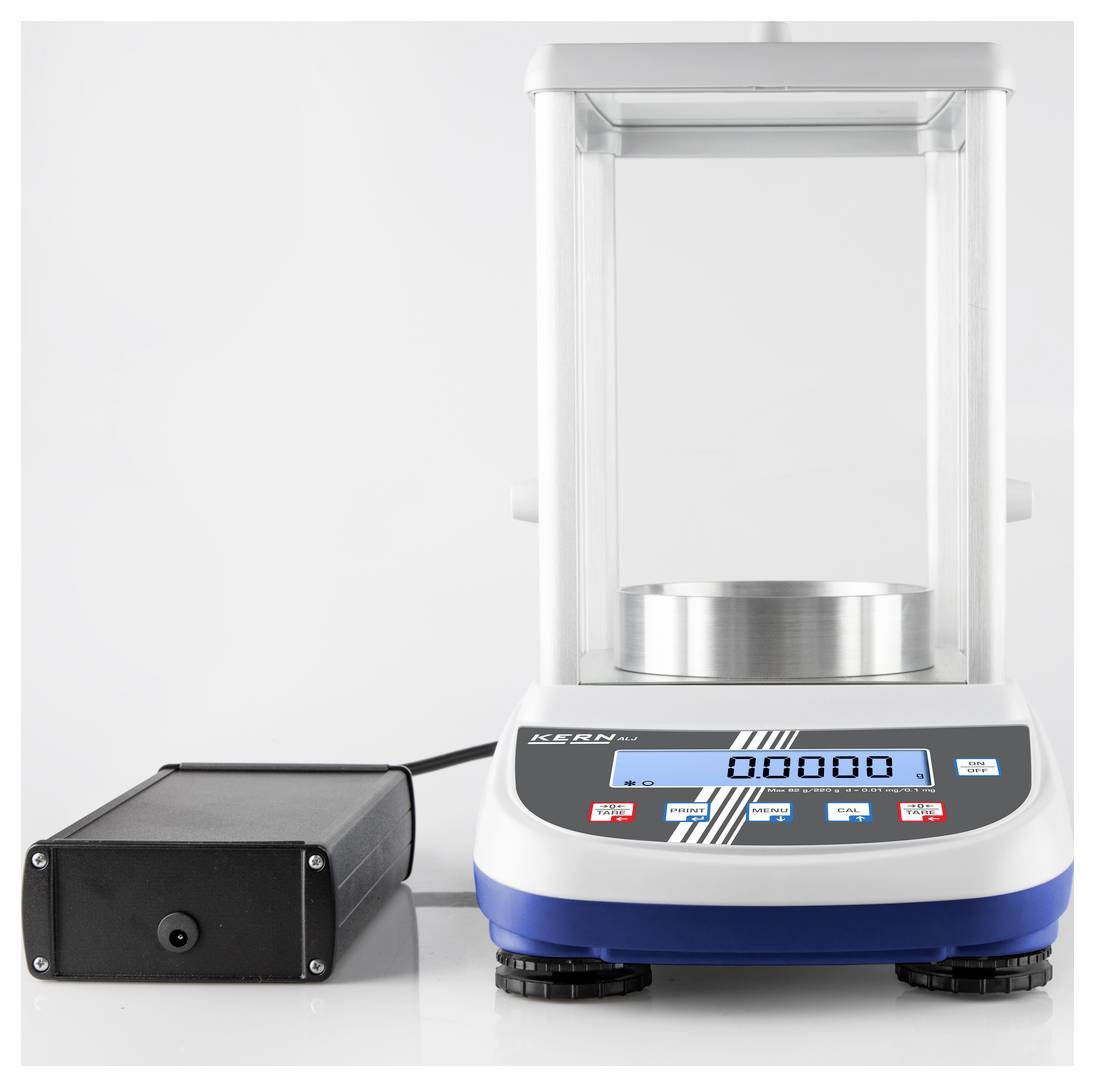 Elektronická přesná váha s digitálním displejem a ovládacími tlačítky. Zobrazuje '0,0000'. Zařízení je připojeno k síťovému adaptéru.