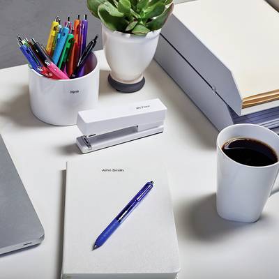 Psací stůl s tužkami, poznámkovými lístečky, rostlinami a šálkem kávy. Kancelářské potřeby jsou uspořádány kolem notebooku.