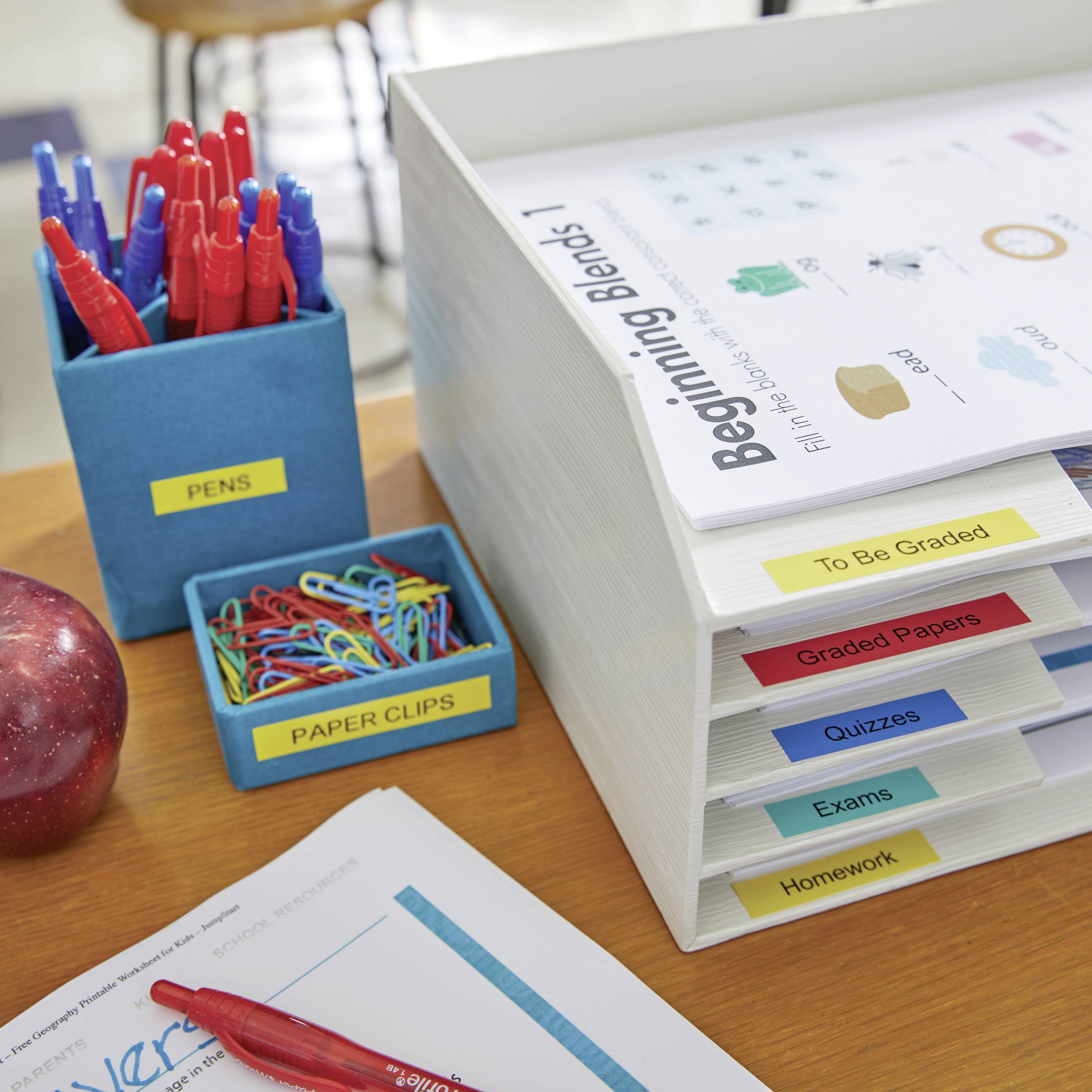 Organizovaná pracovní stanice se sadou odkládacích přihrádek; popisky „K založení", „Hodnocené práce", „Zkoušky"; červené pero, kancelářské sponky.