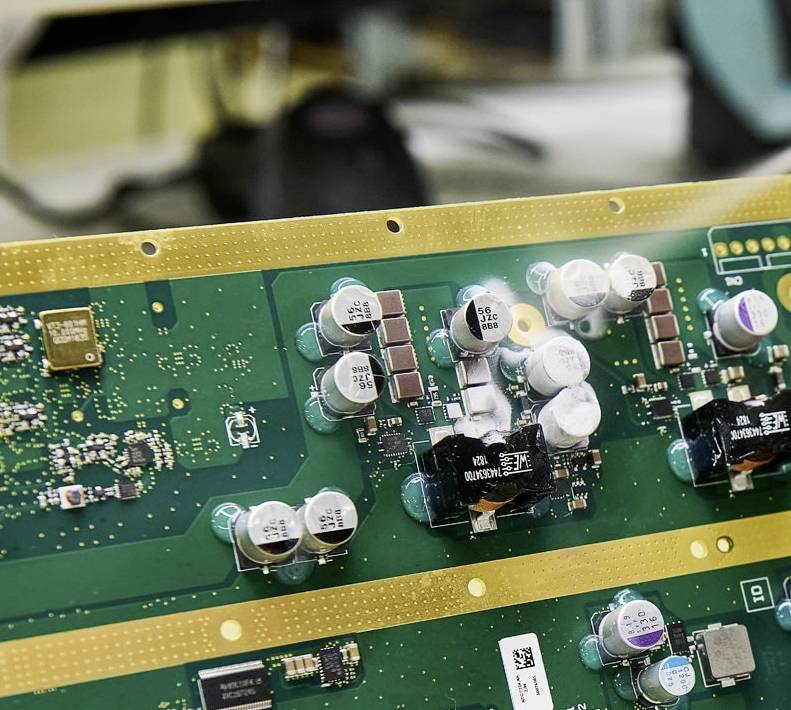 Zelená deska plošných spojů s několika kondenzátory a mikročipy, které jsou součástí elektronického zařízení.