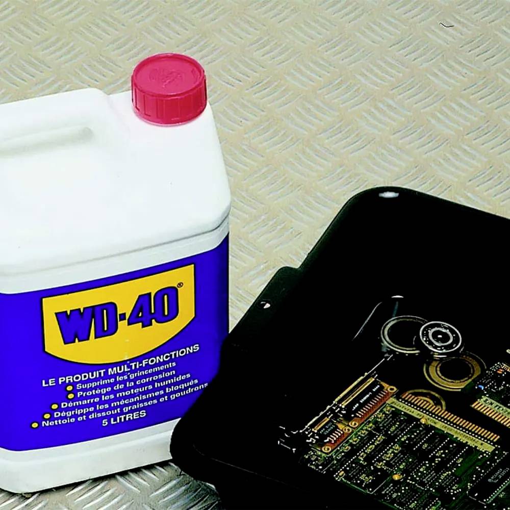 Nádoba WD-40 vedle krabice s elektronickými komponenty na kovovém pozadí.