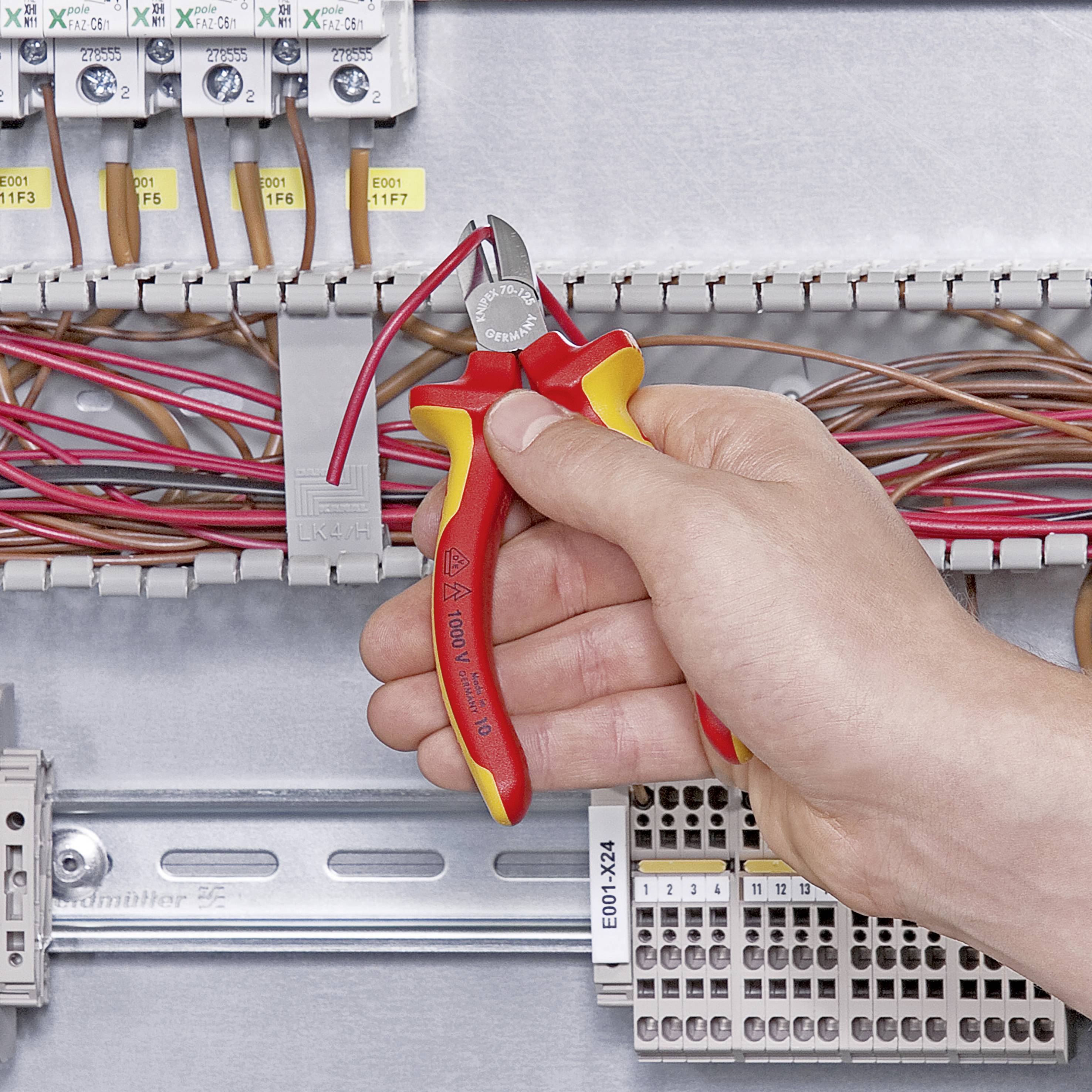 Jedna ruka drží červené štípací kleště, které jsou použity k přestřižení kabelu v pojistkové skříni.