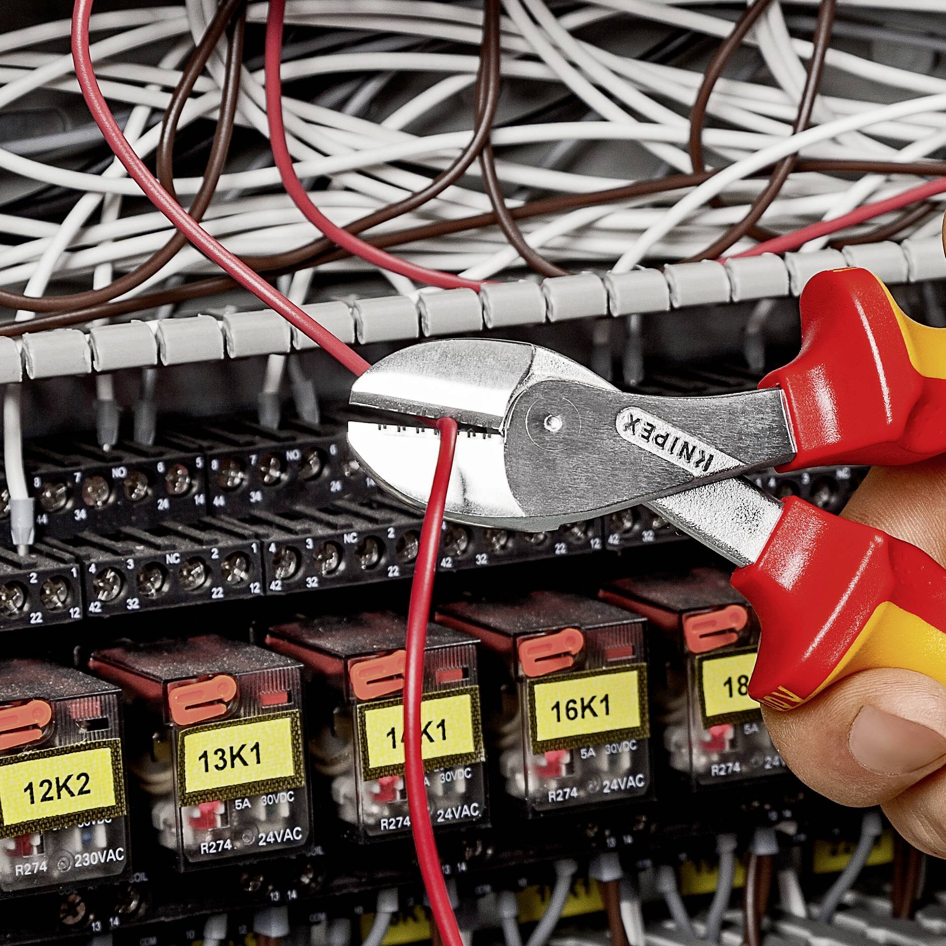 Detailní záběr rukou, které kleštěmi štípají červený kabel z rozvodné skříně.