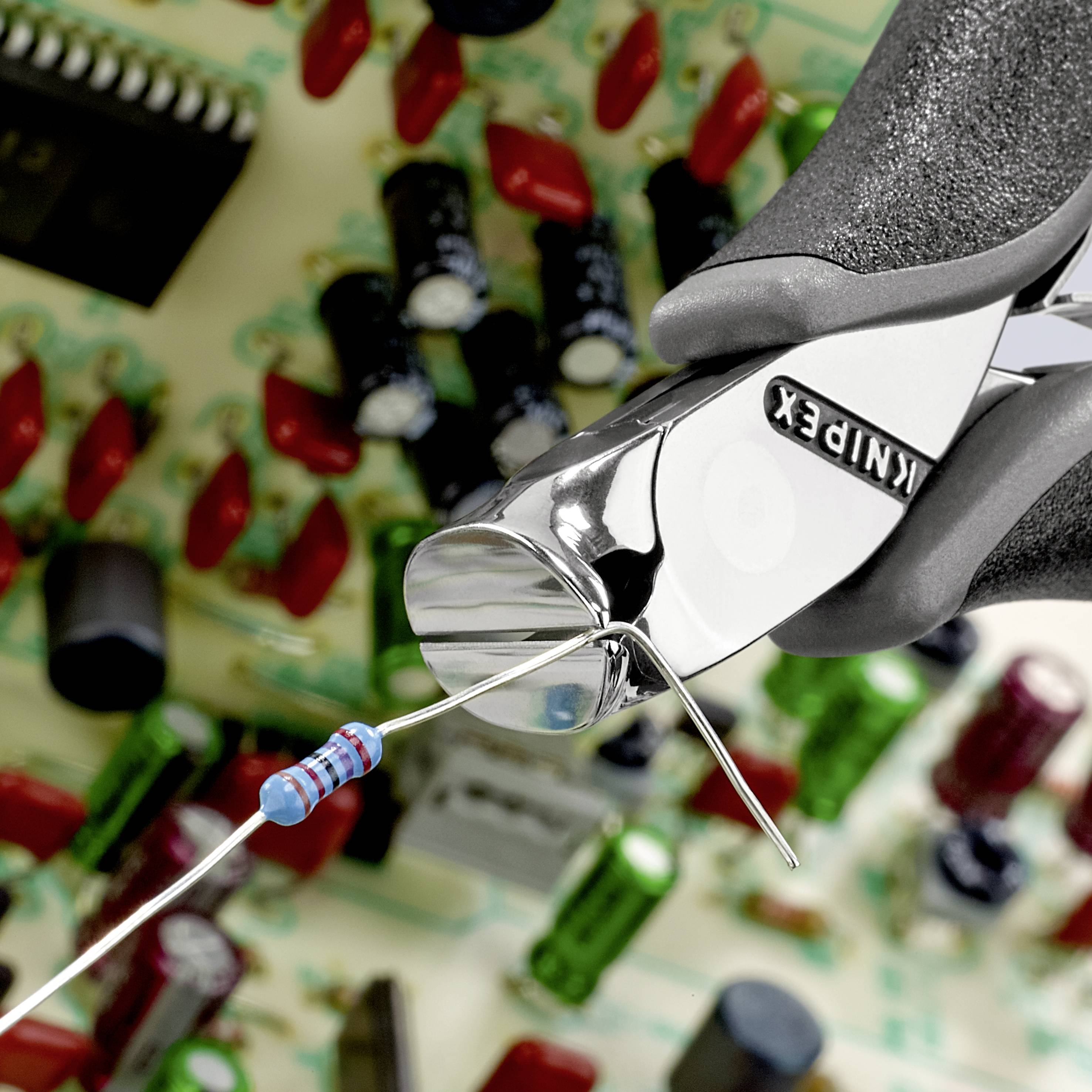 "Štípací kleště stříhají vývodní nožičku odporu", v pozadí deska plošných spojů s různými elektronickými součástkami.