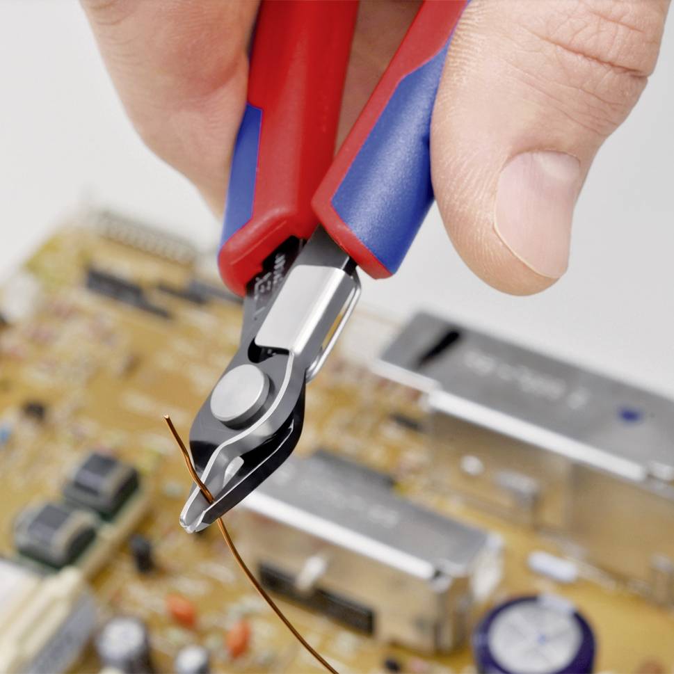 Jedna ruka drží boční štípací kleště, které přestřihávají tenký kabel nad elektronickou deskou.